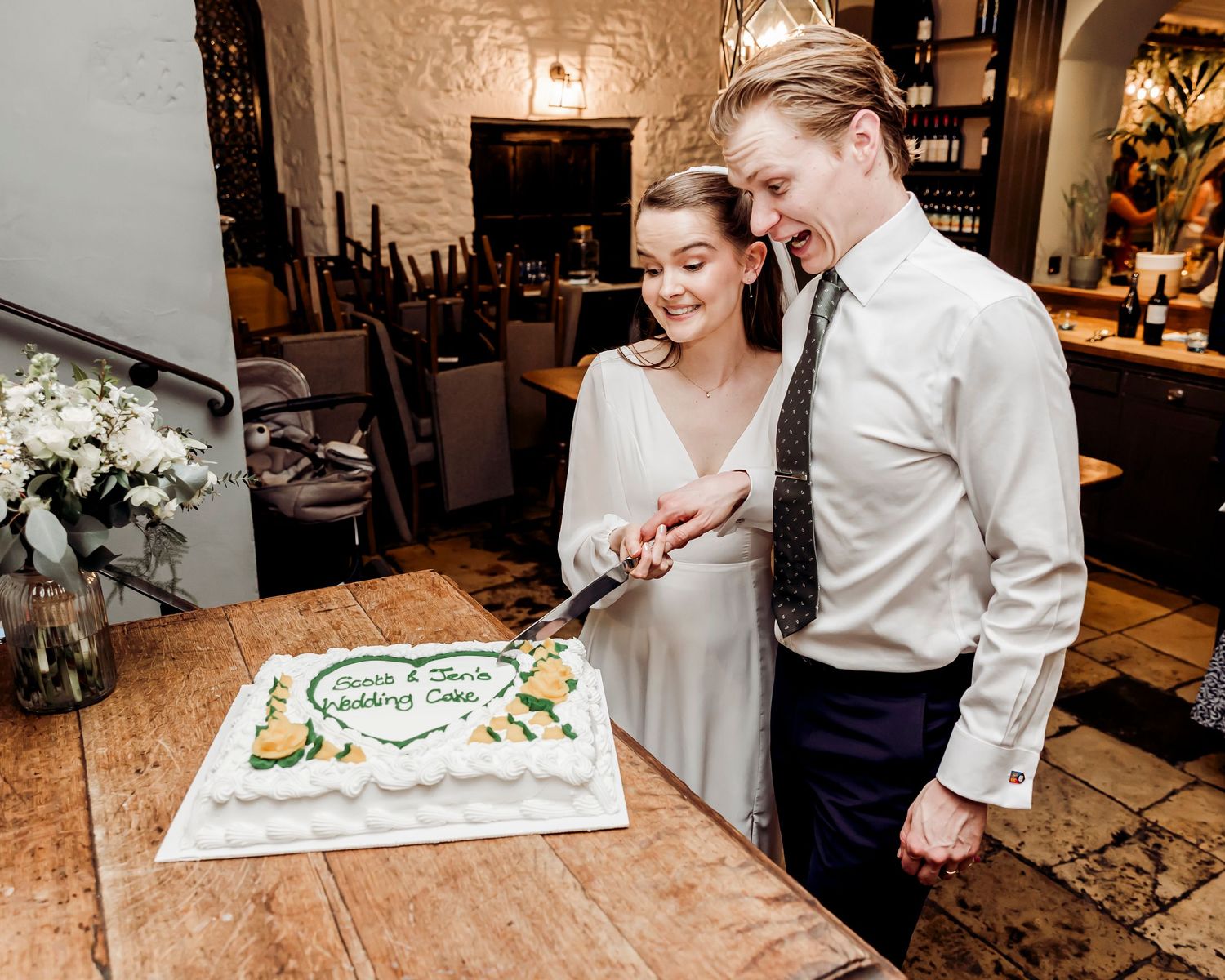 Bride and groom cutting their decorated white wedding cake together at reception.