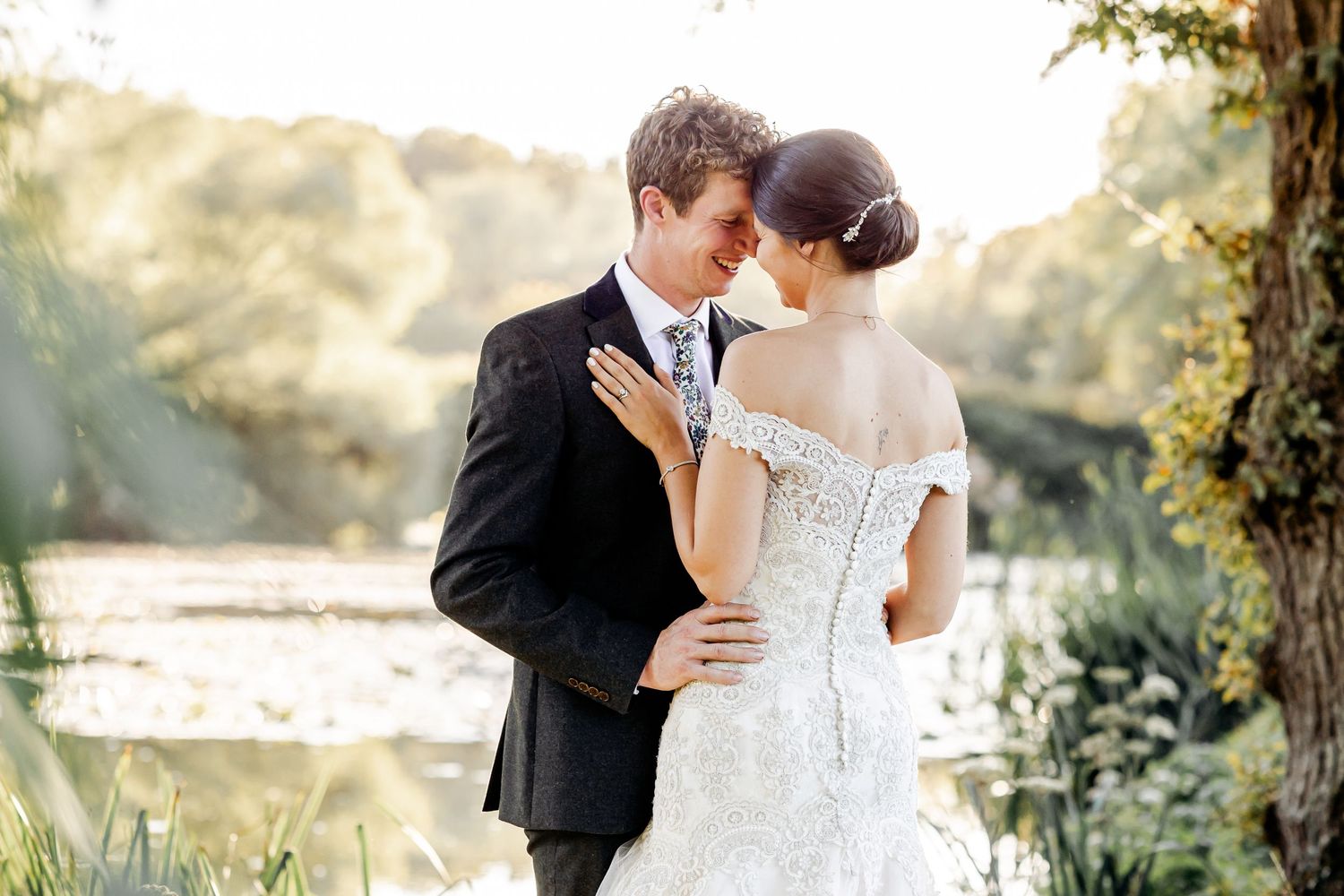 Bride and groom sharing a romantic moment near a sunlit river during portraits.