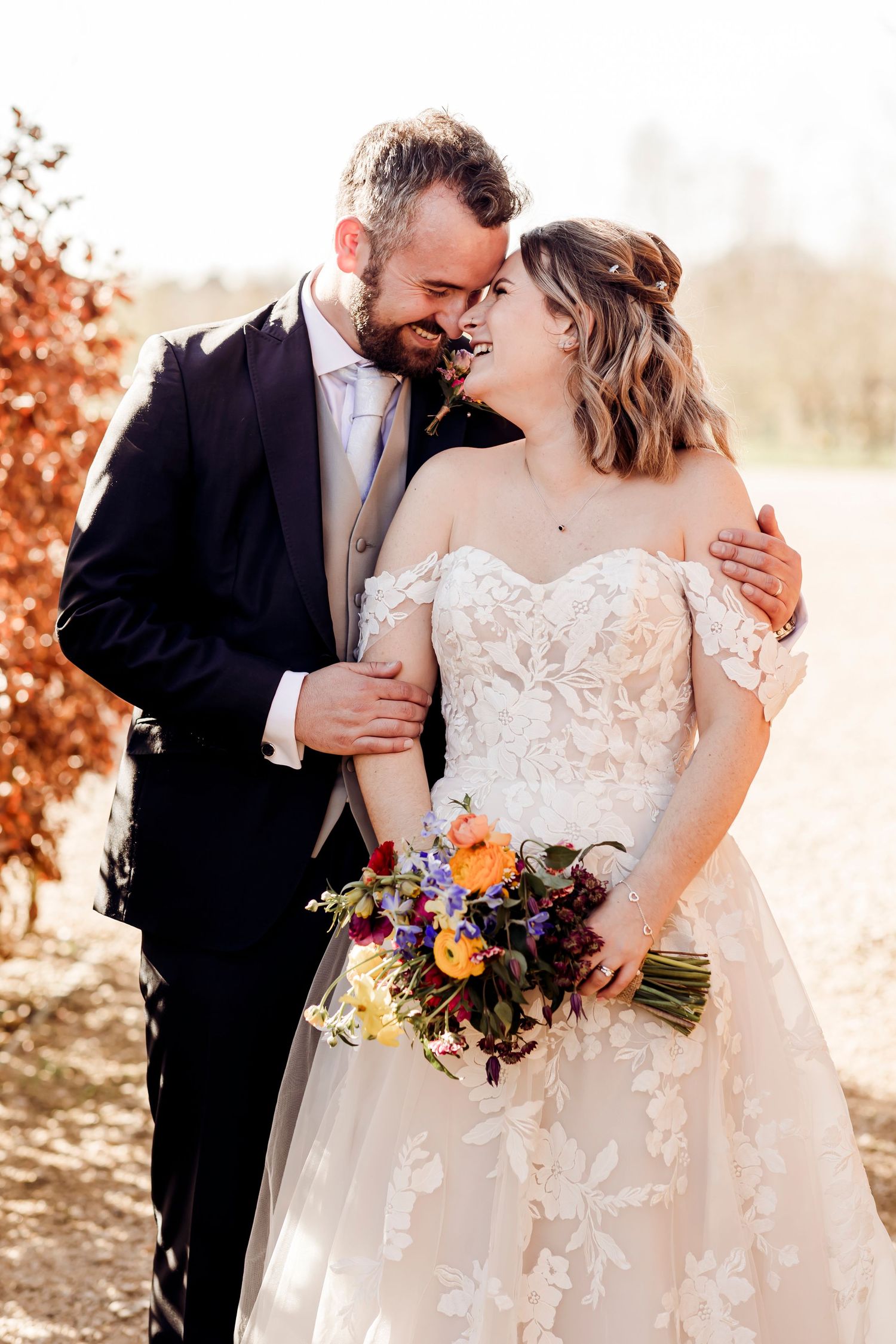 Bride and groom share tender moment outdoors, bride holding colorful bouquet in autumn setting.