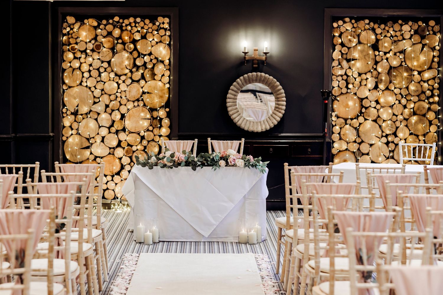Elegant wedding ceremony venue with log wall backdrop, chiavari chairs, and floral sweetheart table.