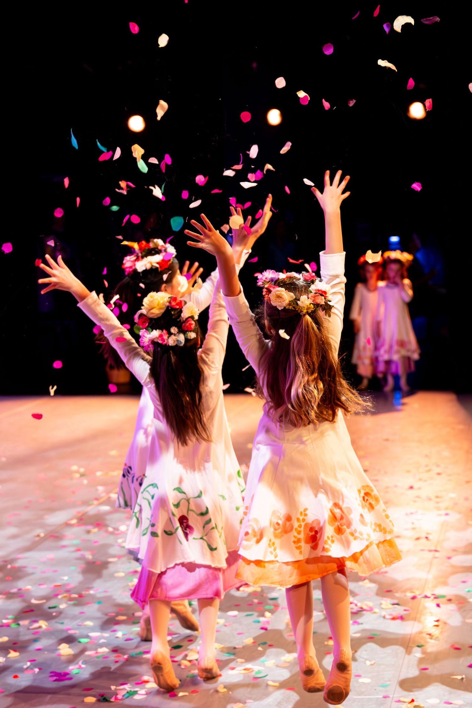 Young dancers in pink costumes perform on stage as colorful confetti rains down during a joyful dance recital.