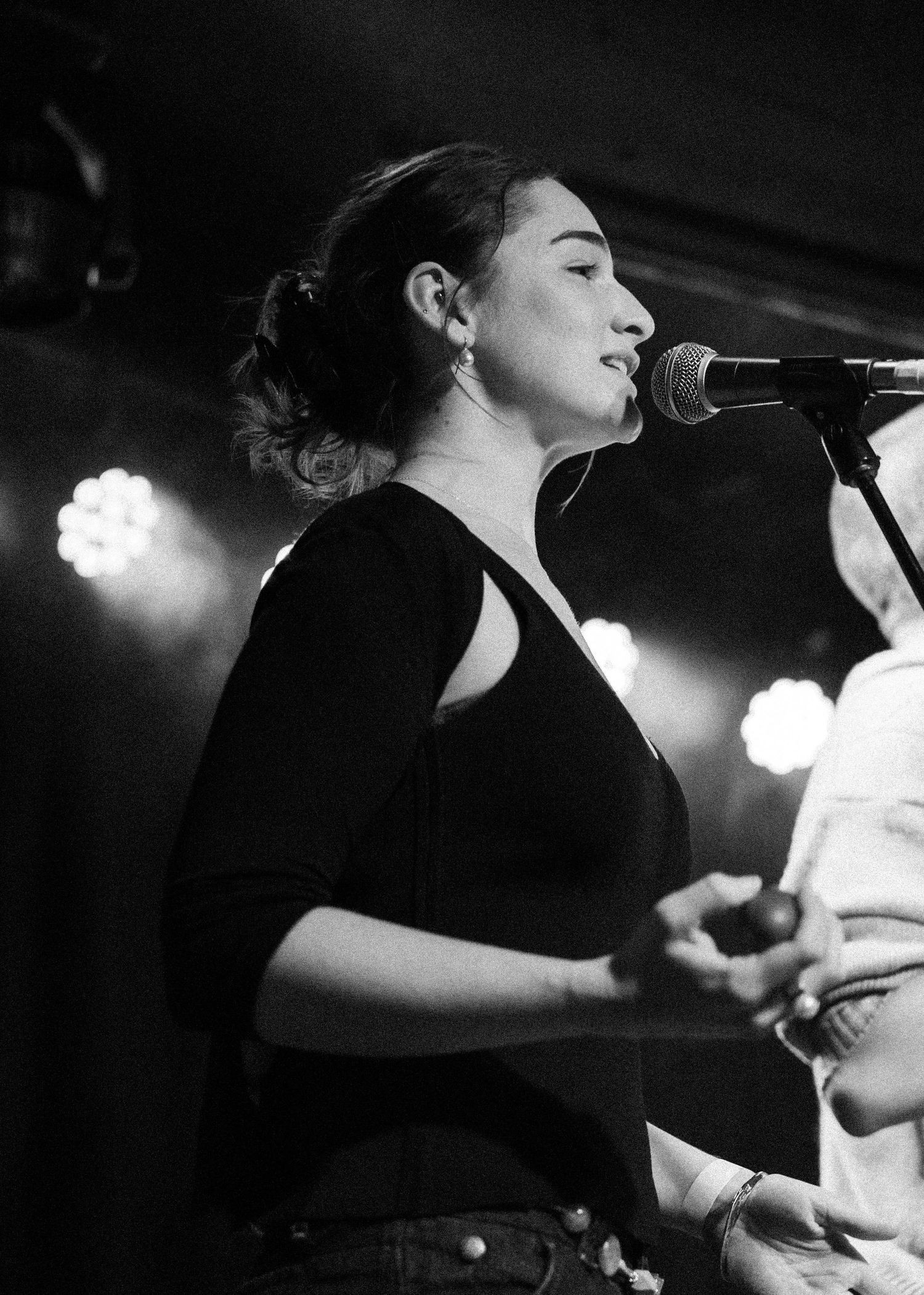 Black and white photo of a young woman singing into a microphone on stage under bright lights.
