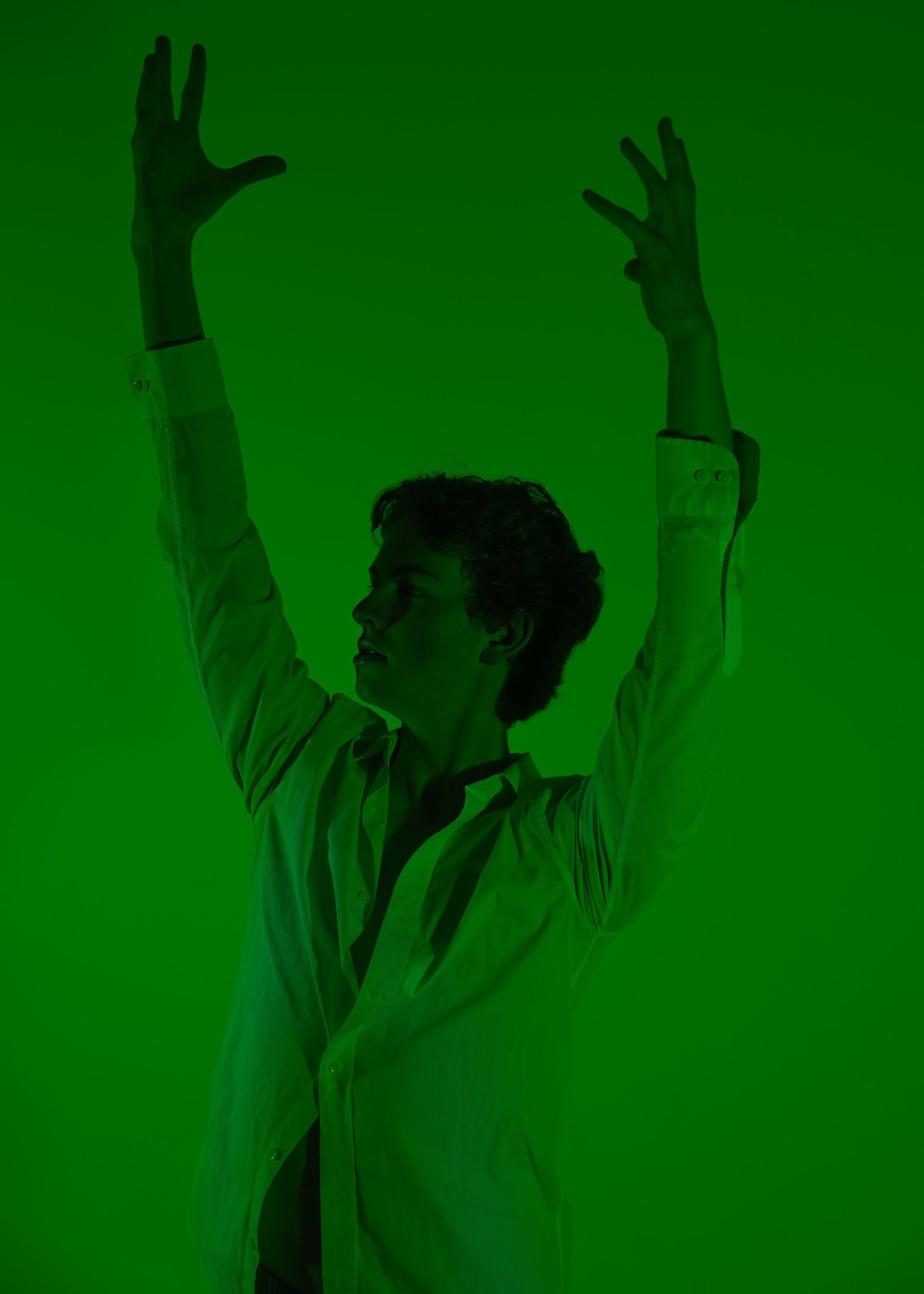 Dancer poses dramatically with arms raised against a vibrant green background in a white blazer.