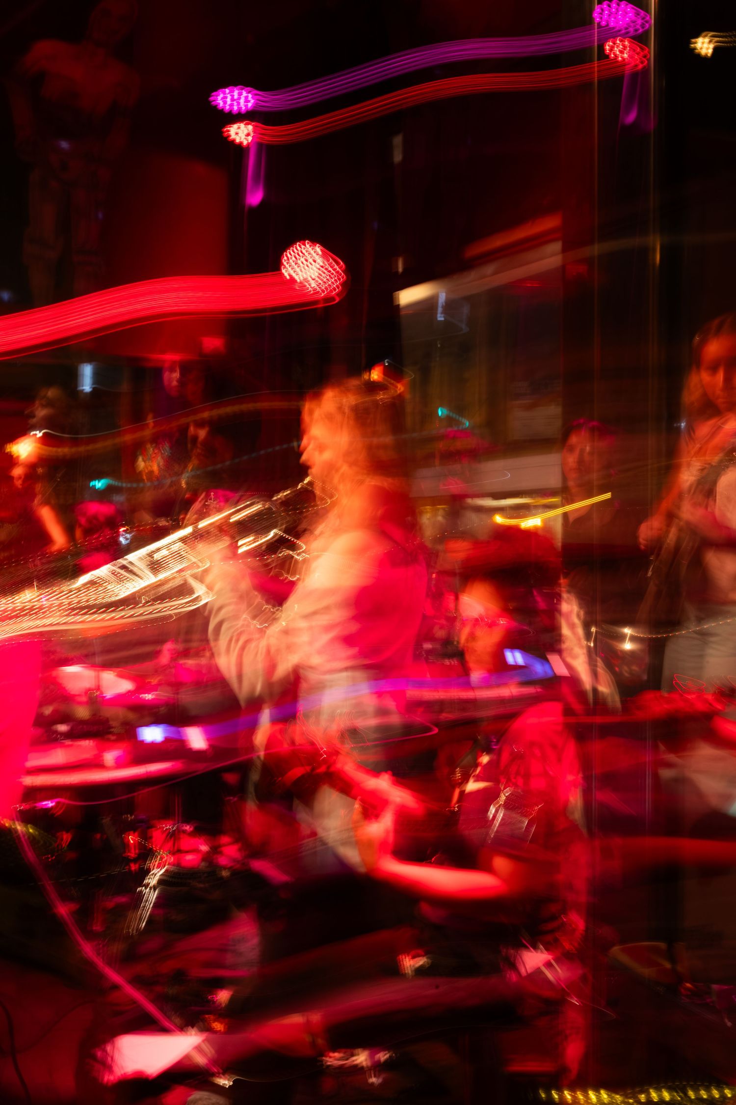 Long exposure photograph captures the energy of musicians performing in a red-lit club setting.