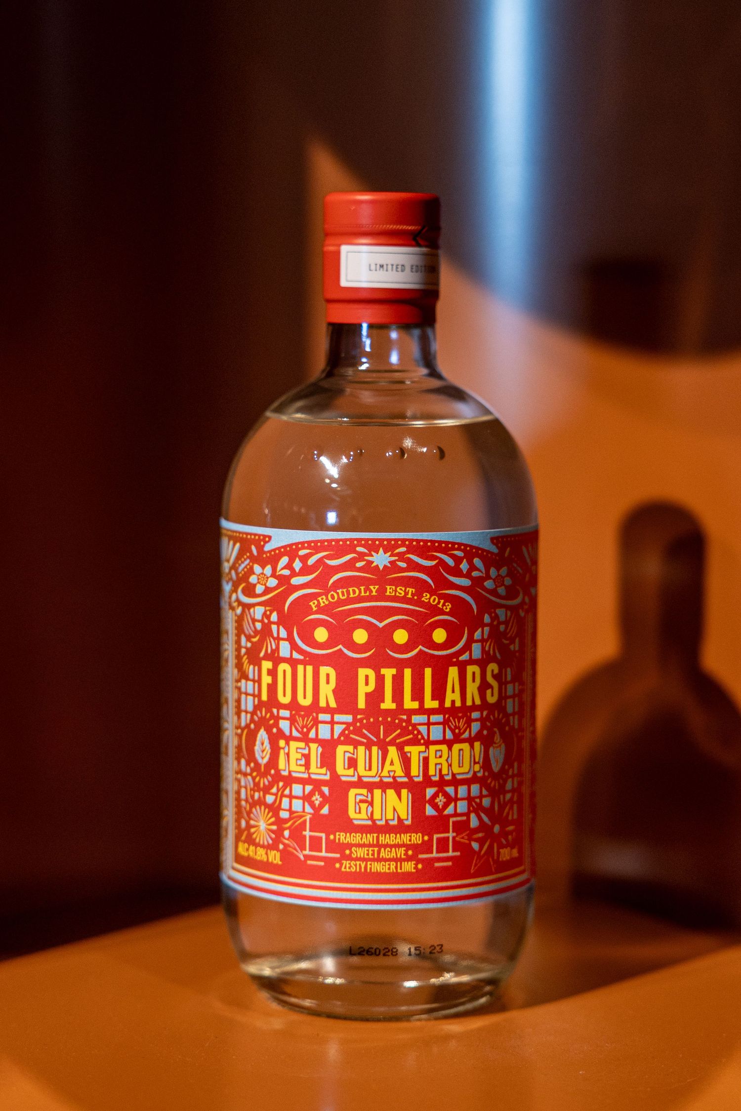 Four Pillars El Cuatro Gin bottle with vibrant red label and red cap displayed on a wooden shelf.
