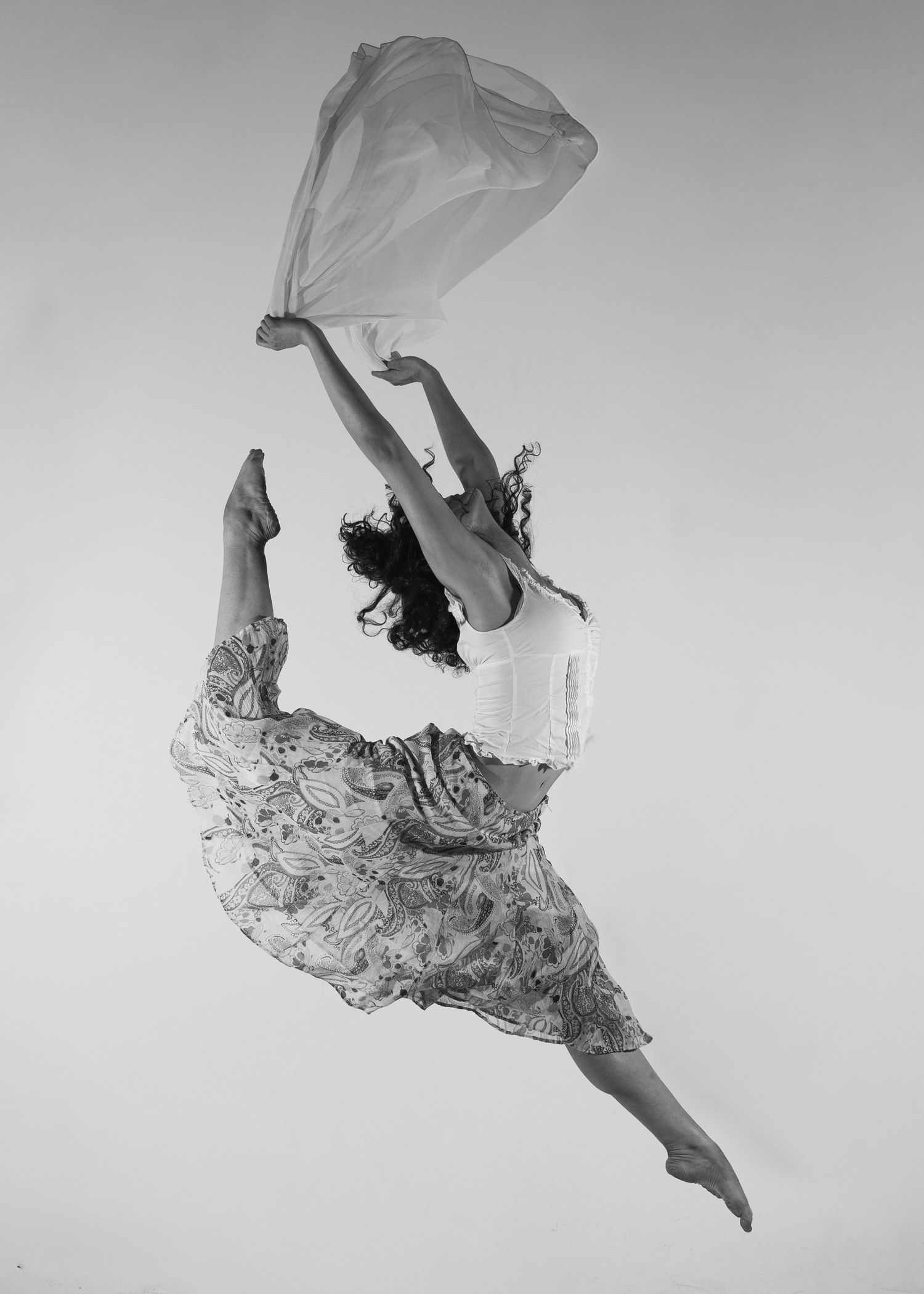Dancer leaping gracefully mid-air holding flowing fabric in black and white photo.