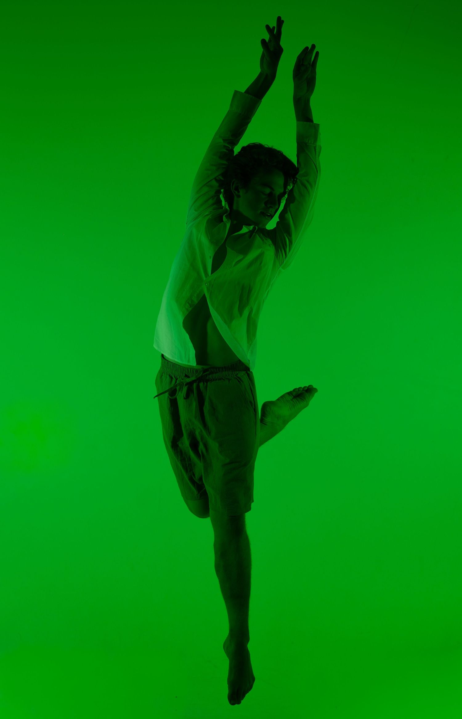 A dancer leaps gracefully against a vibrant green background, arms raised overhead in an expressive contemporary dance pose.