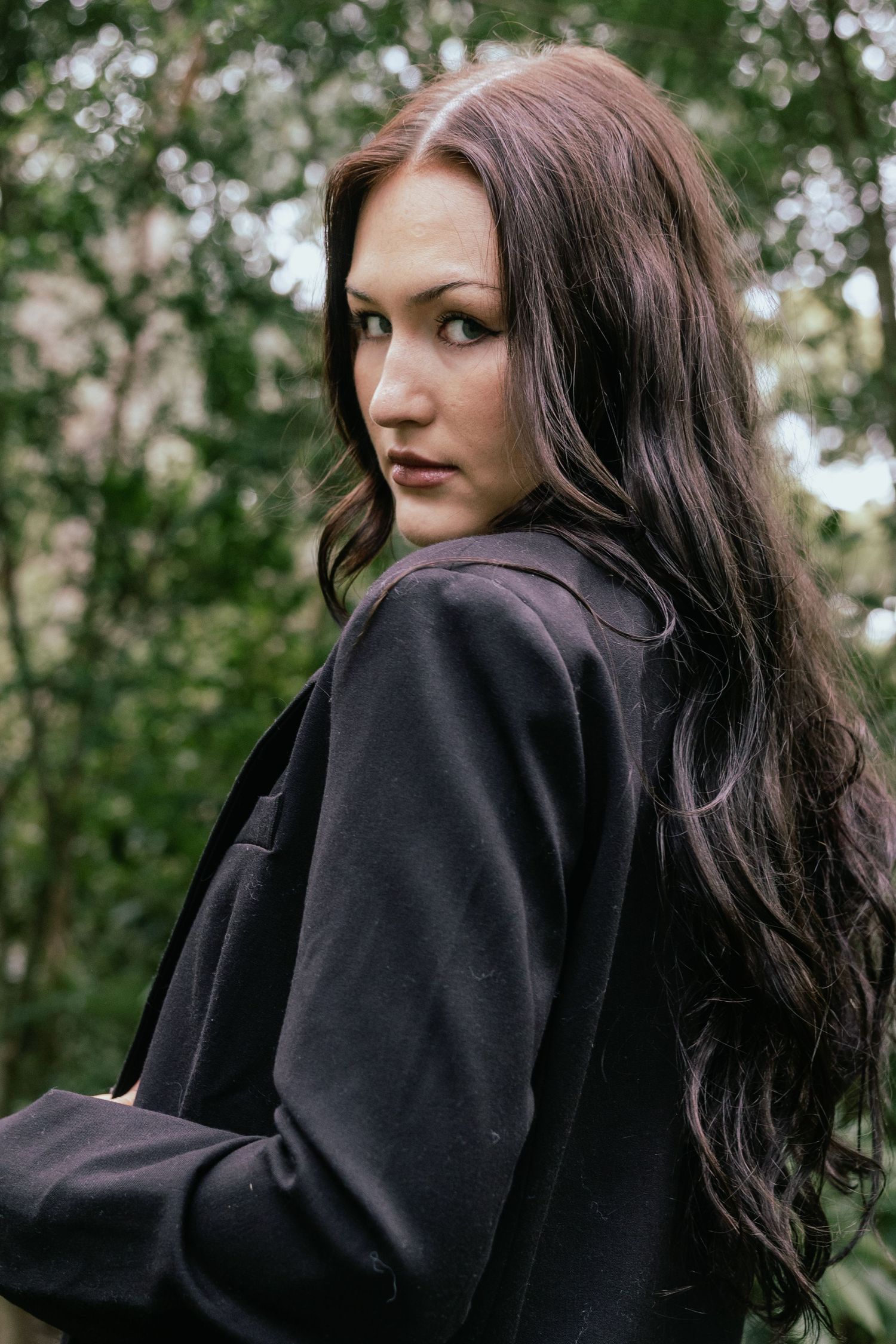 Young woman in black jacket with long hair in forest.