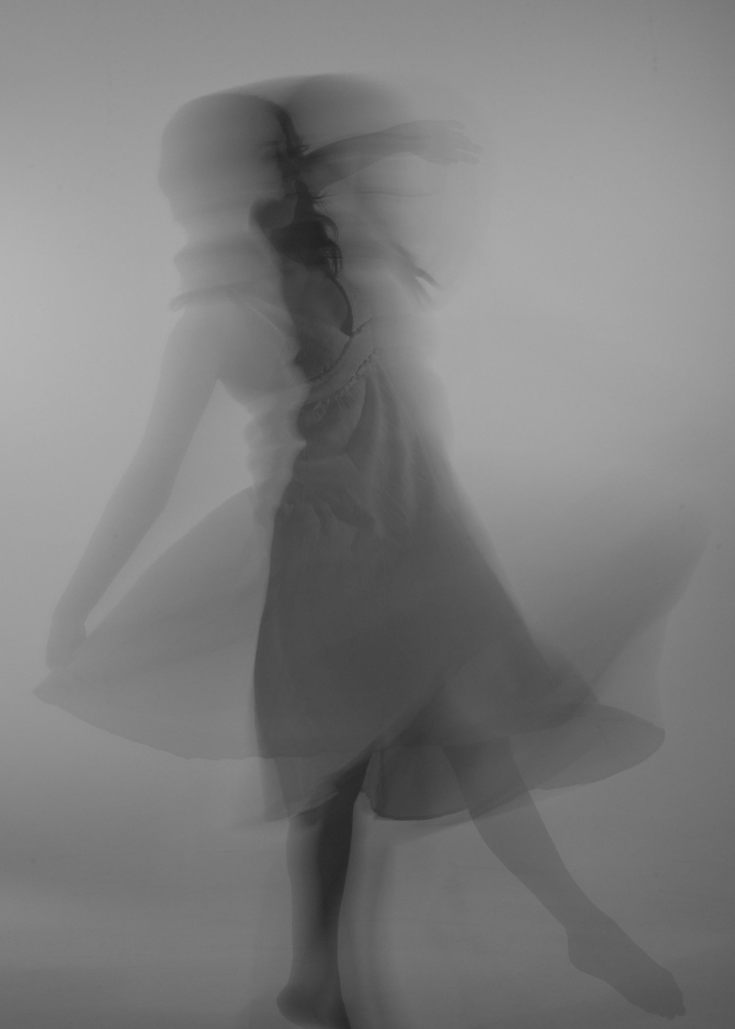 Blurred black and white long exposure photo of a woman in a dress dancing gracefully.