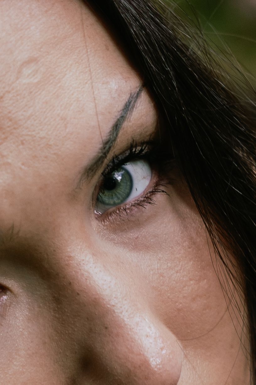 Close-up of a woman's green eye with dark eyebrow and long lashes, natural skin texture visible.