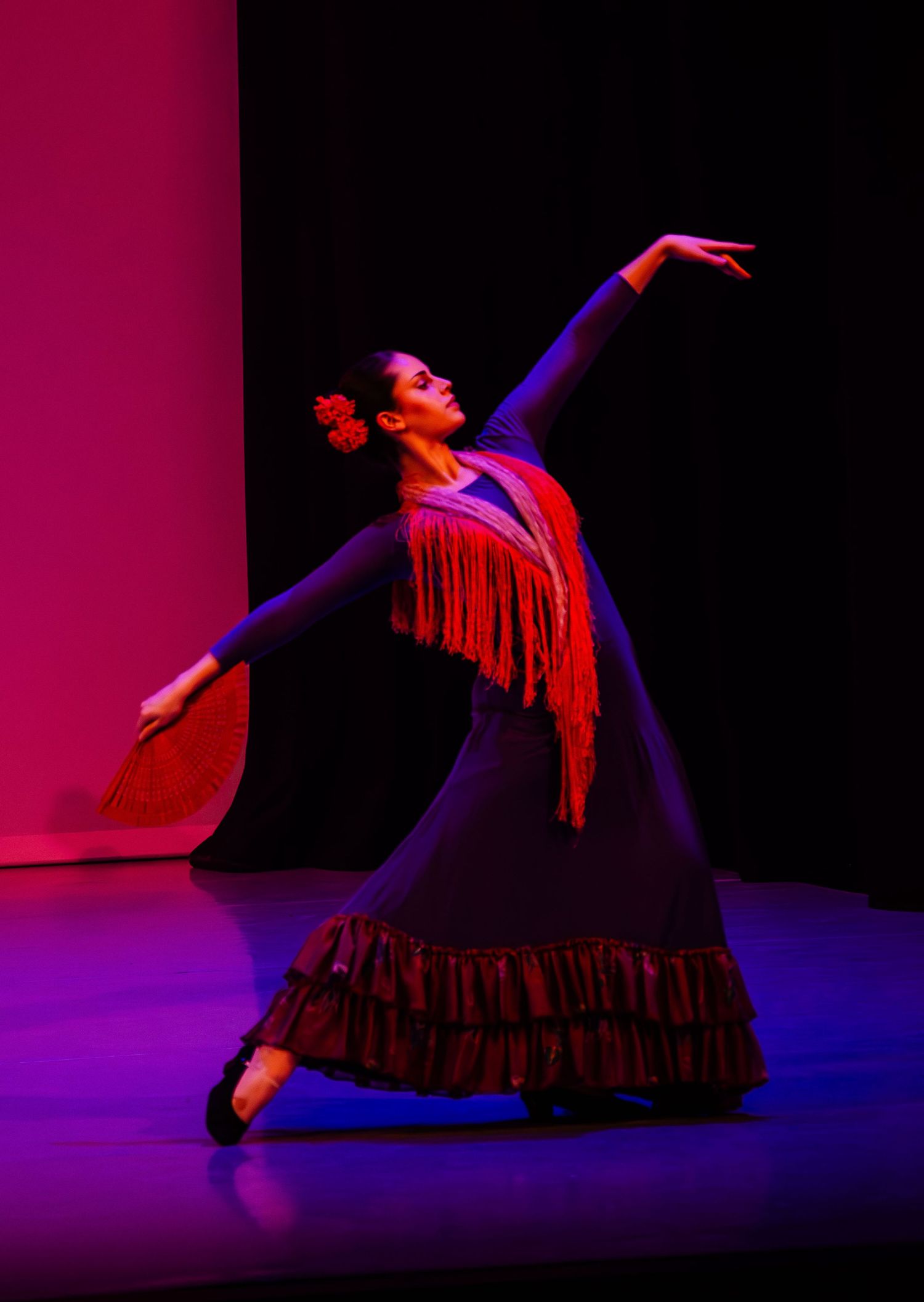 Dramatic silhouette of a dancer in a ruffled dress performing against vibrant pink and blue stage lighting.