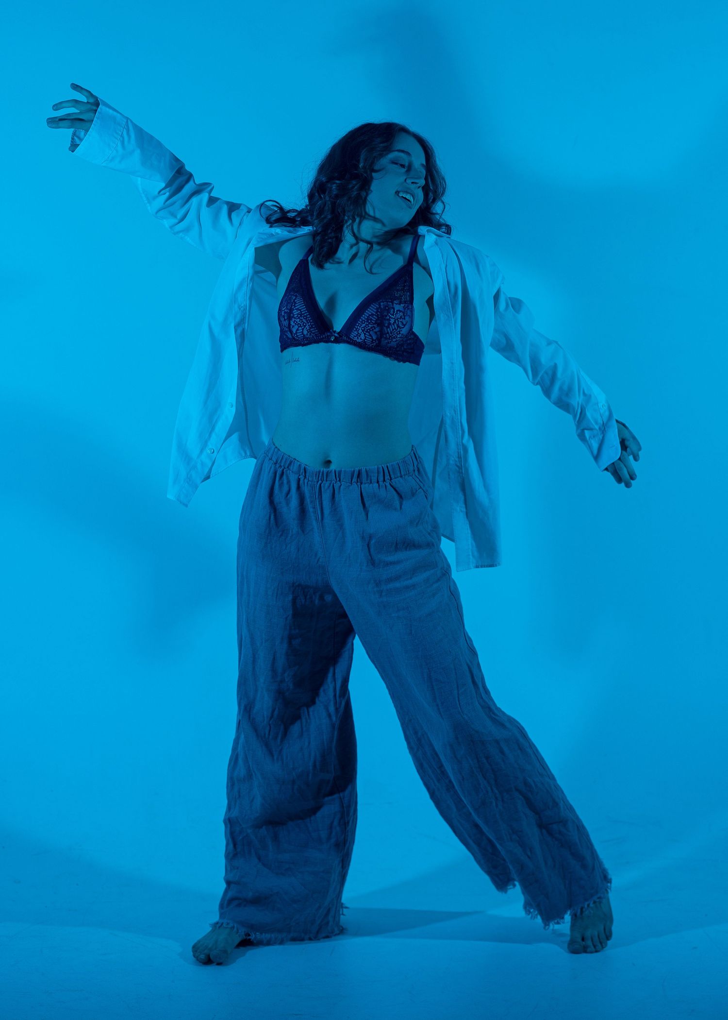 Dancer posing dramatically under blue lighting wearing wide-leg pants and a sequin bralette with arms outstretched.