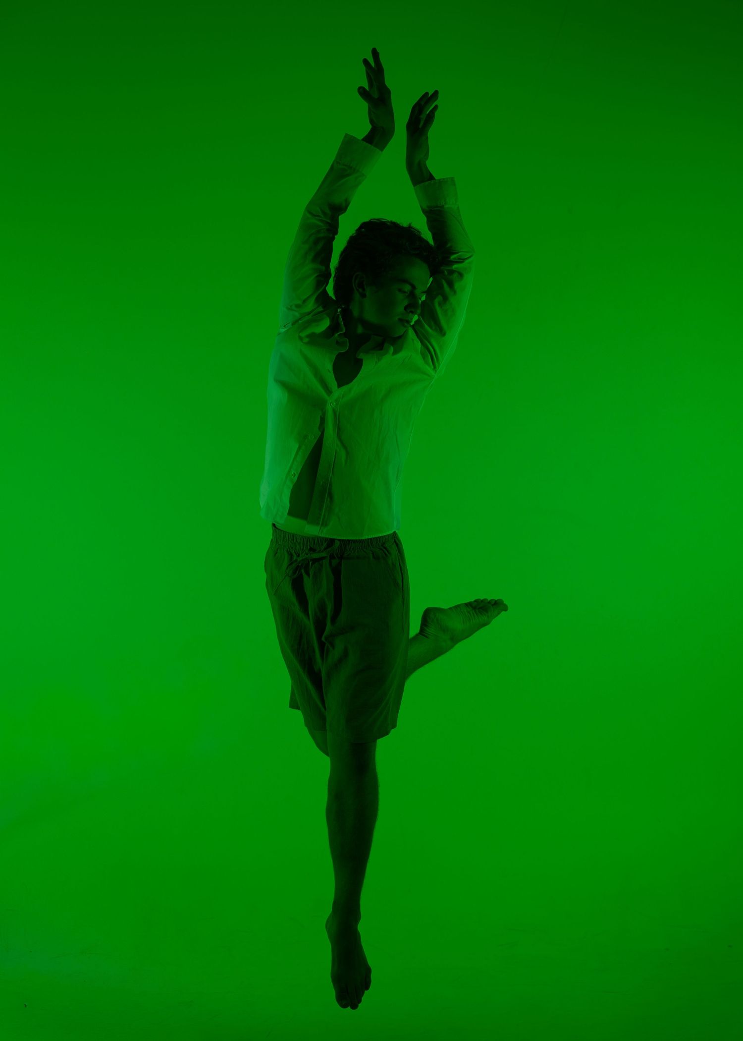 A dancer leaps gracefully against a vivid green background, arms raised overhead in an expressive contemporary dance pose.