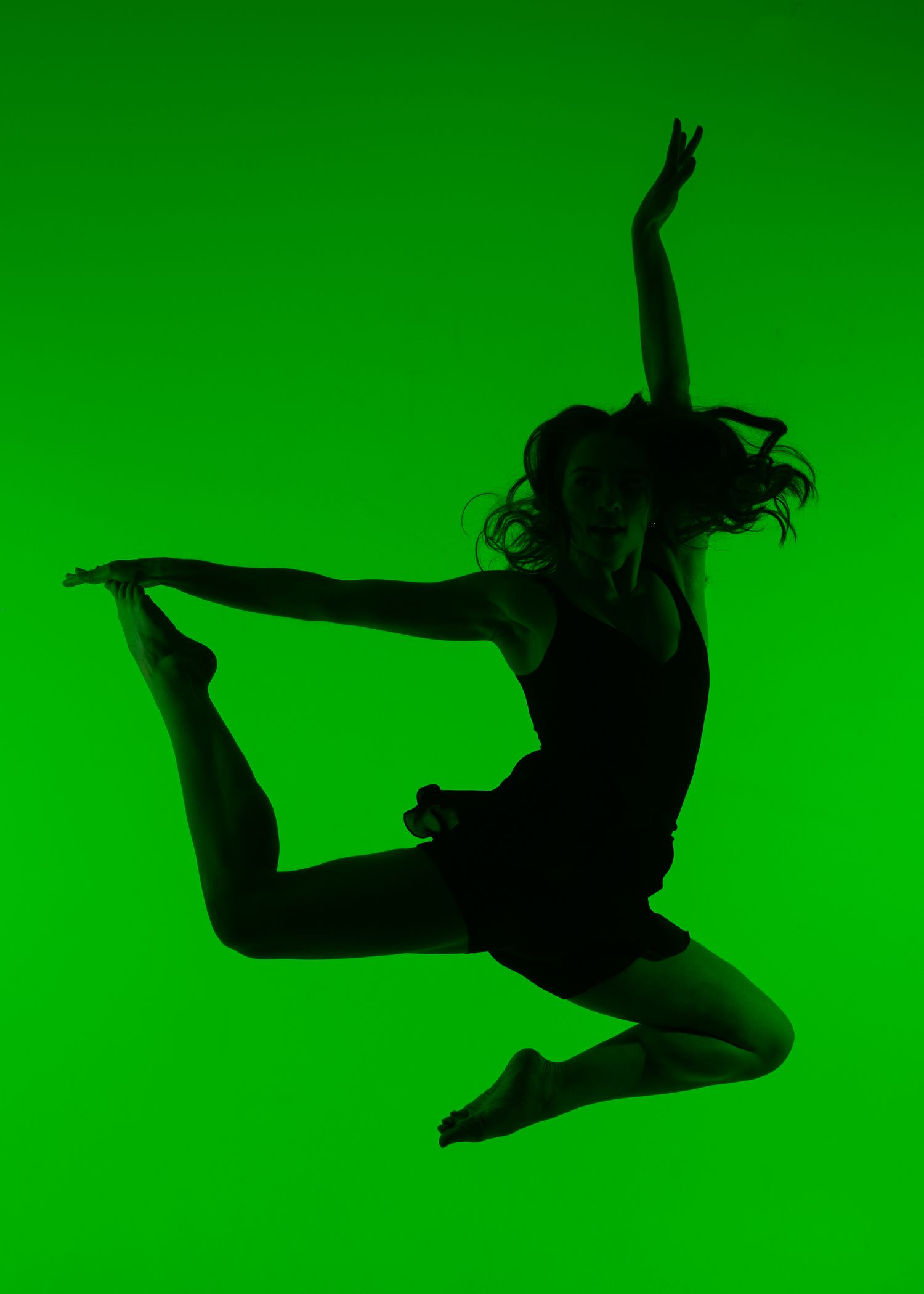 Silhouette of a dancer leaping gracefully against a vibrant green background in a dynamic pose.
