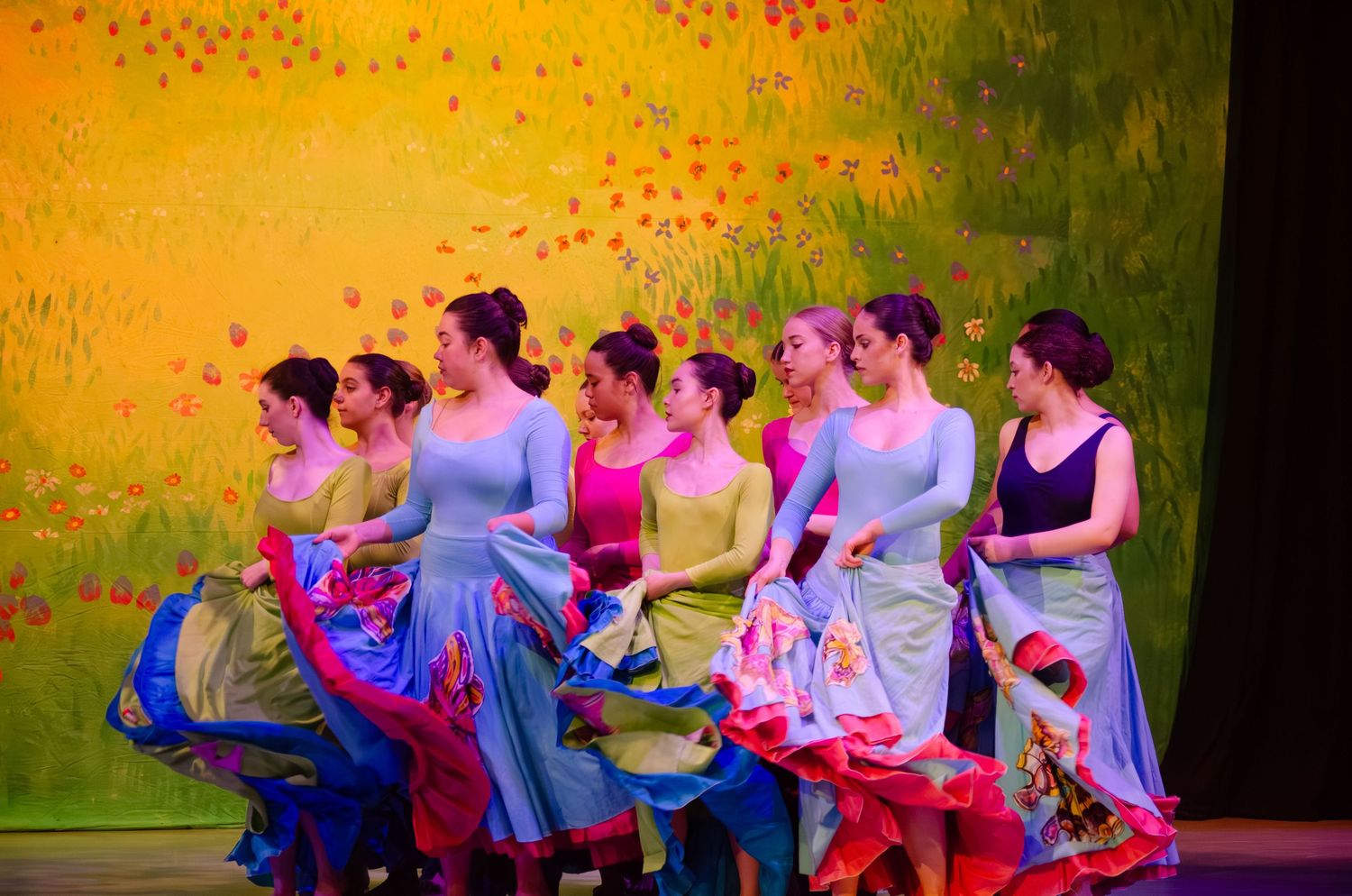 Dancers perform a colorful group dance routine on stage wearing vibrant pink and blue costumes.
