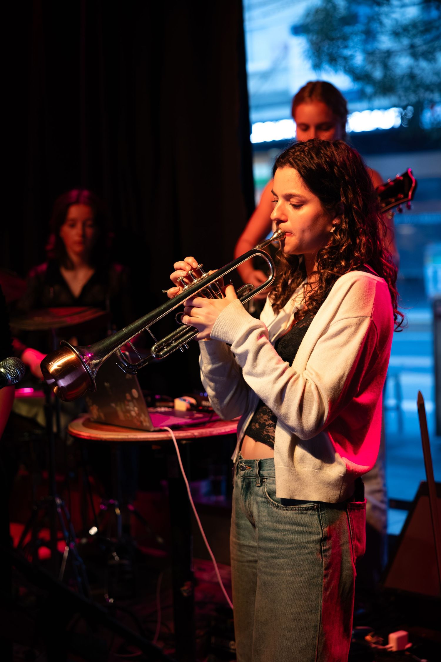 A musician performs on stage with a trumpet under dramatic red and blue lighting at a jazz club performance.