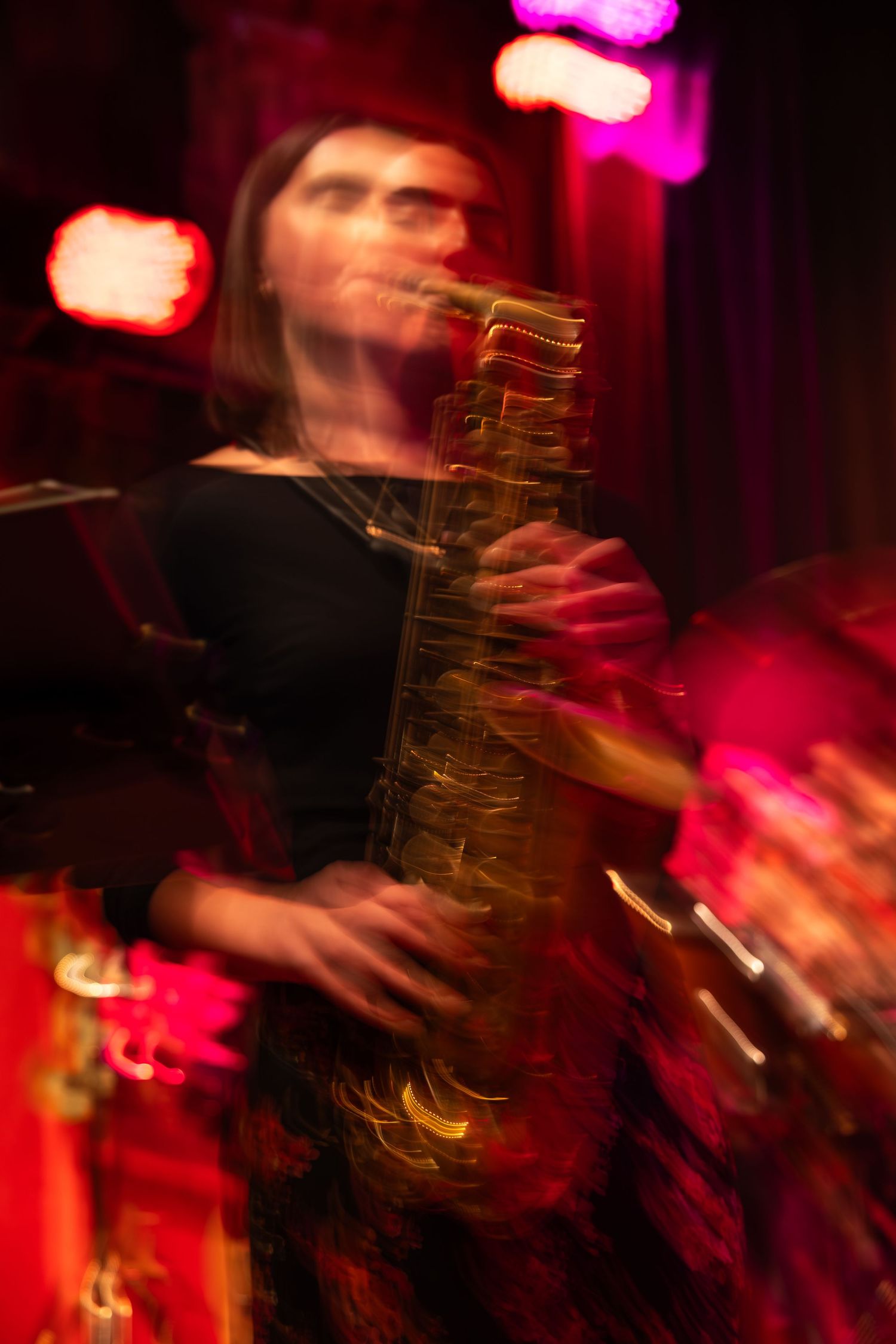 Motion blur captures a musician performing on stage with vibrant pink and red lighting creating a dynamic atmosphere.