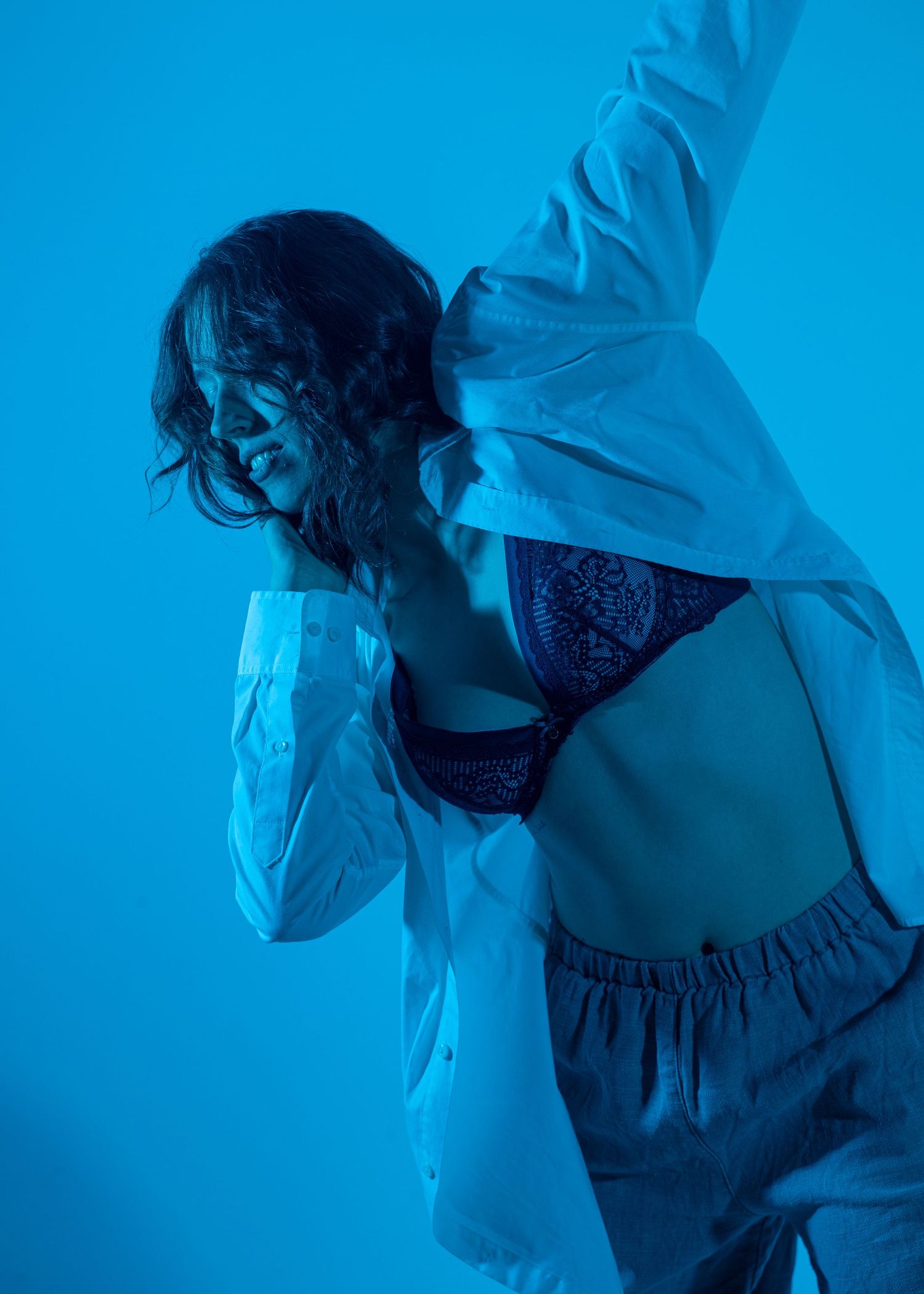 Dynamic dancer in a white shirt and dark bra striking a pose under dramatic blue lighting.