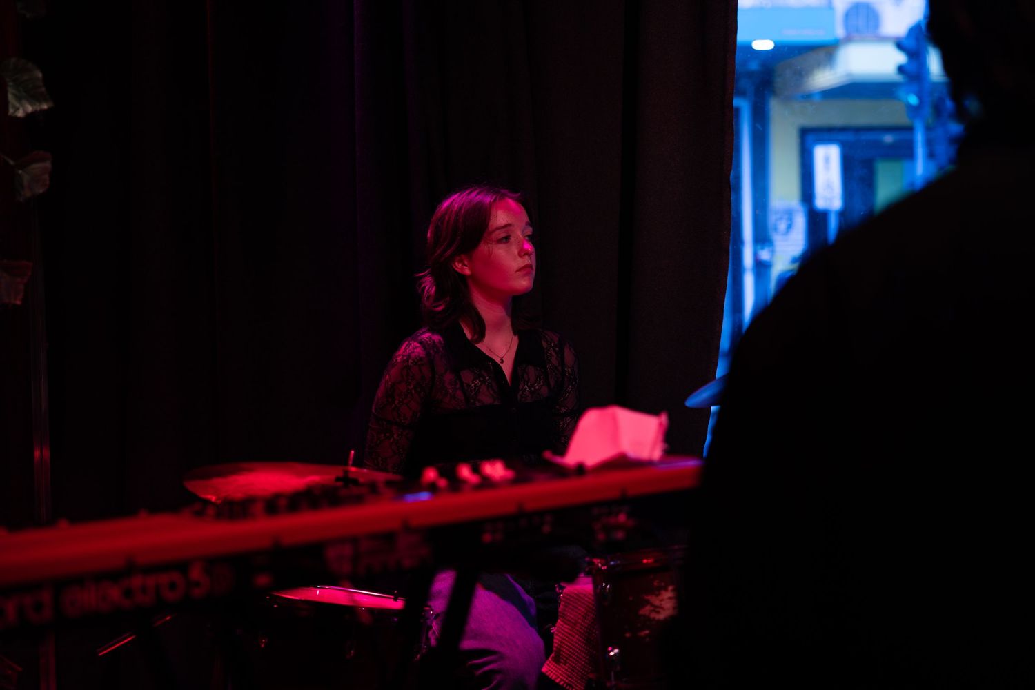 Musicians perform on stage under dramatic red lighting during a live concert performance.