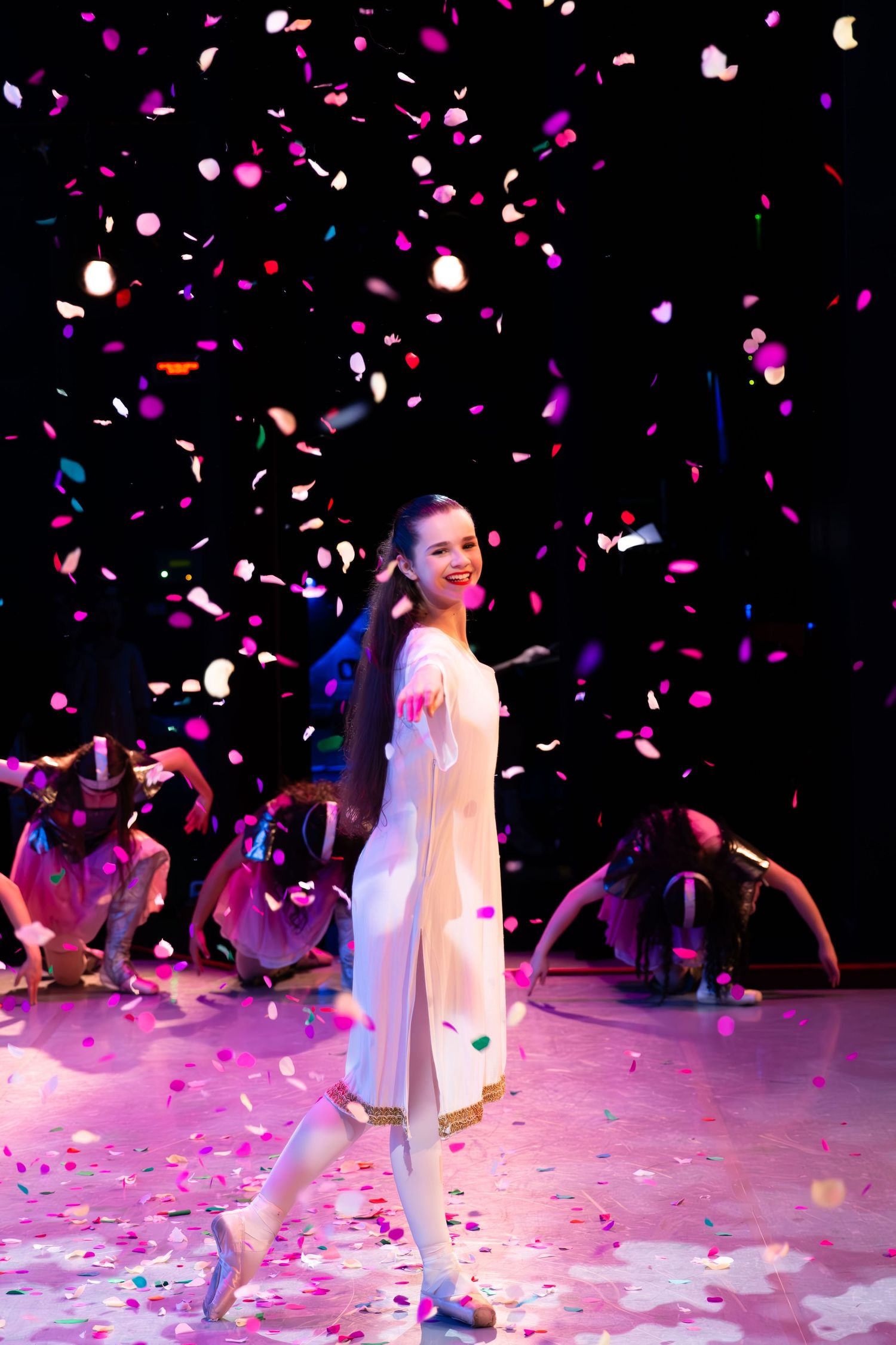 A performer in white stands on stage while pink and white confetti rains down during a celebratory moment.
