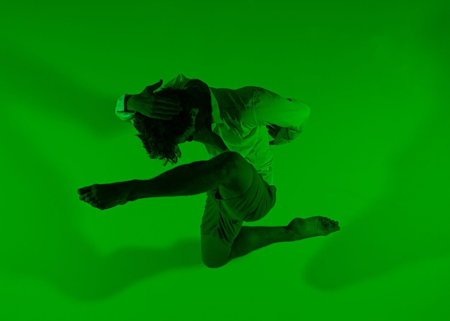Dancer leaping dynamically against a vibrant green background, captured mid-air in an expressive contemporary dance pose.