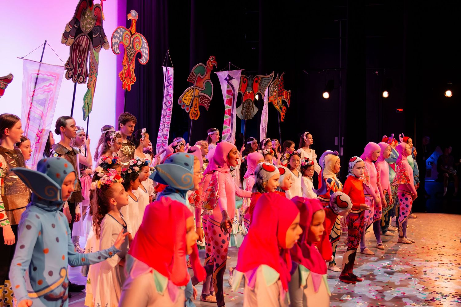Colorful theatrical performance with costumed performers on stage featuring vibrant props and elaborate costumes.
