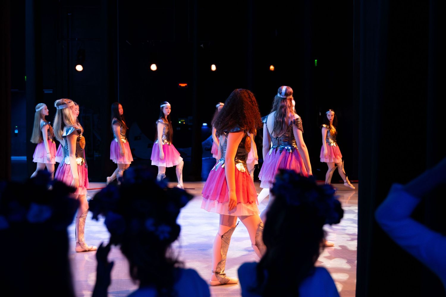 Young dancers perform on stage in colorful tutus under vibrant pink and blue stage lights during a dance recital.