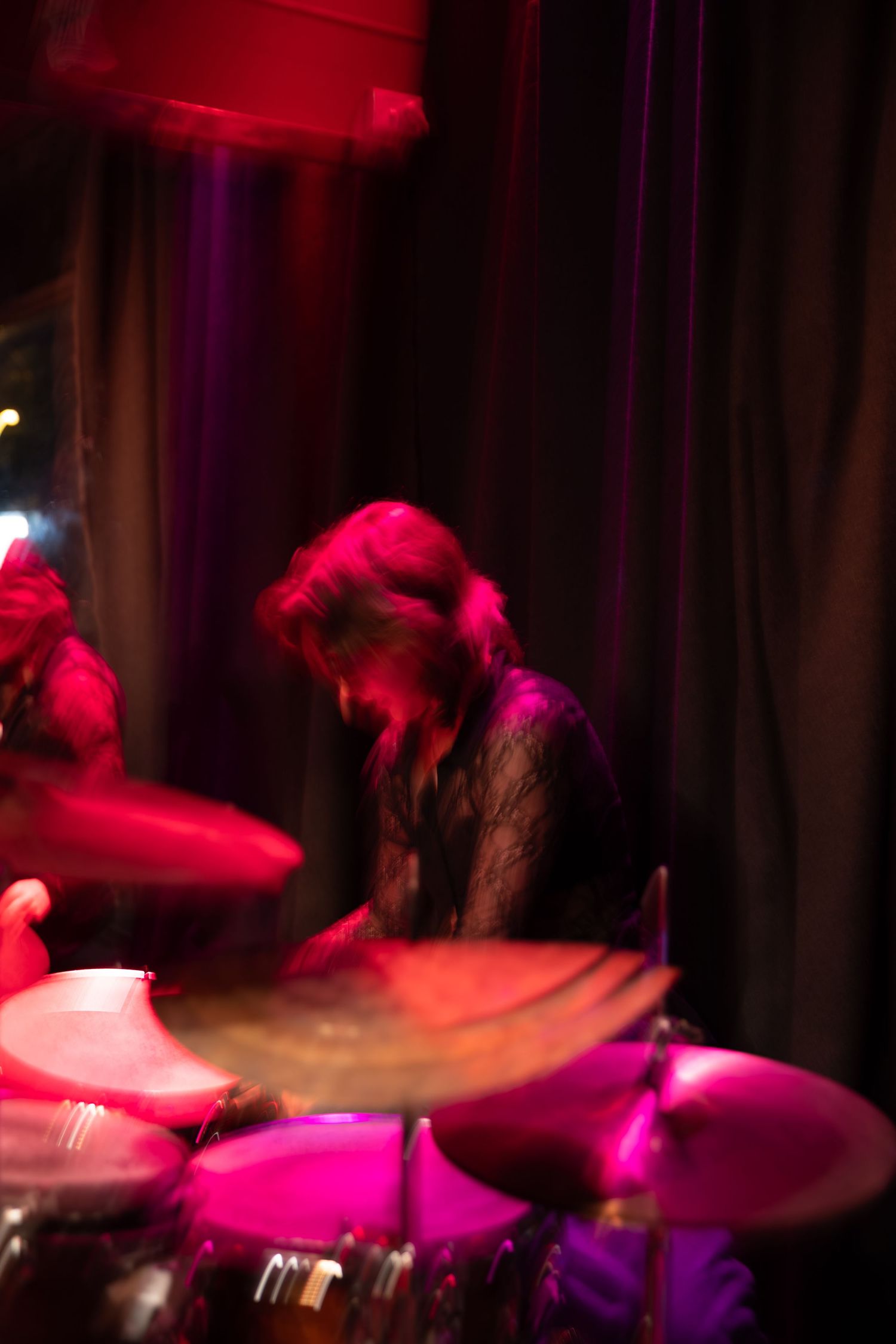 Drum cymbals captured in motion blur under vibrant red and purple stage lights during live performance.
