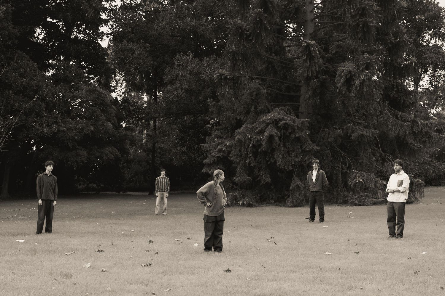 Five people standing apart in an open field with large trees in the background, black and white photo.