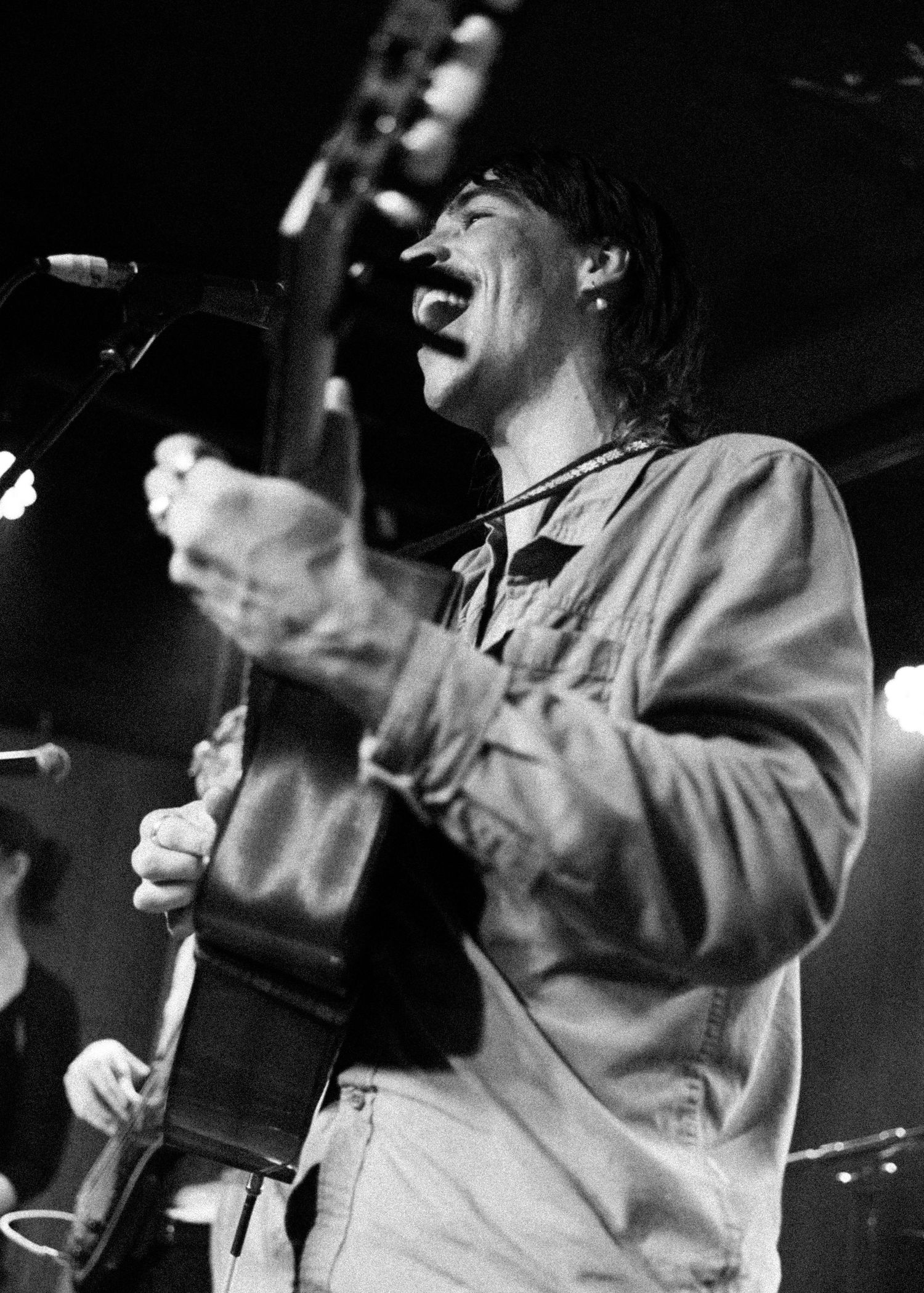 Black and white photo of a musician singing and playing guitar on stage under bright lights.