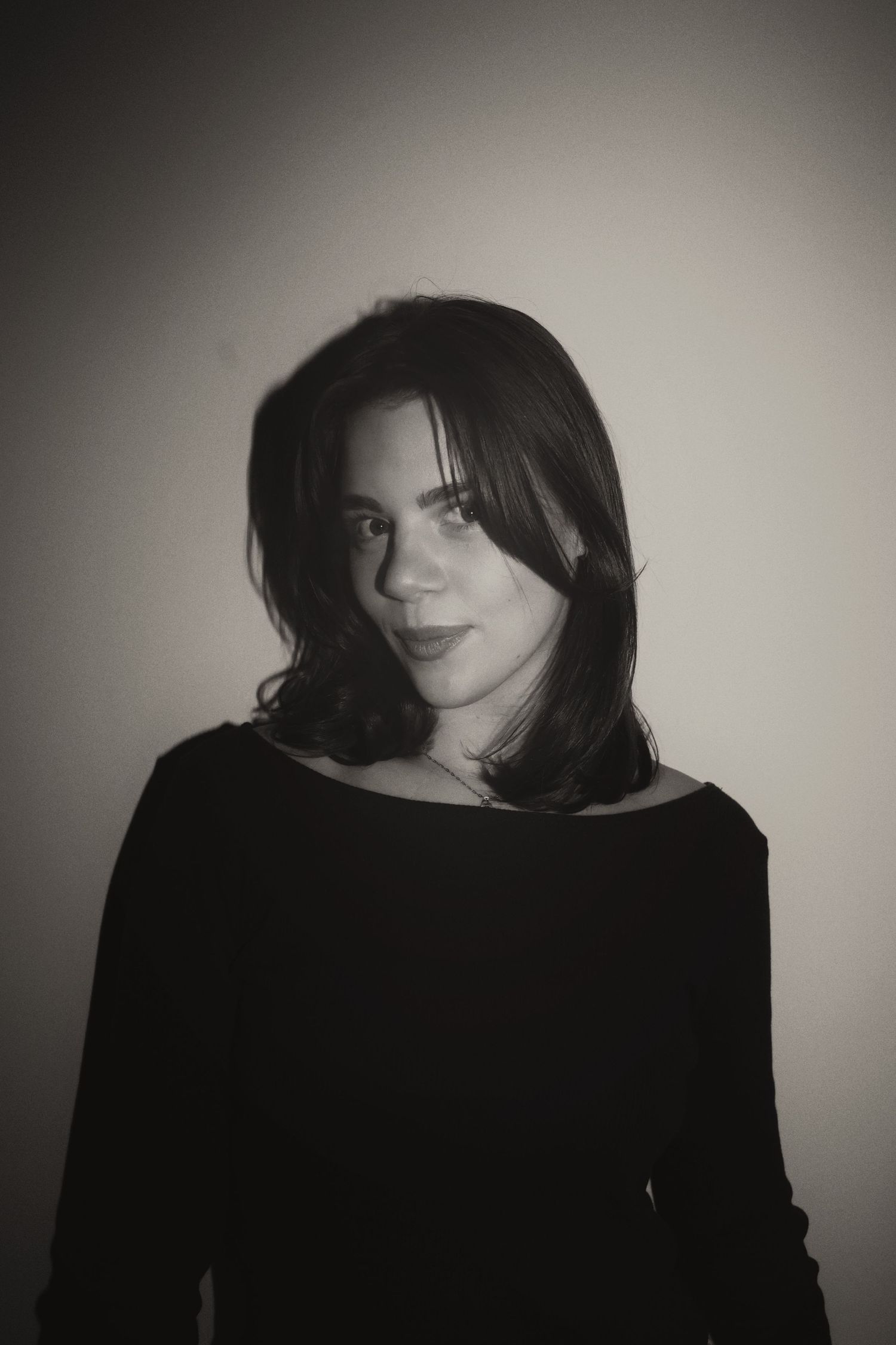 Black and white portrait of a young woman with dark hair wearing a black top, posing against a light background.