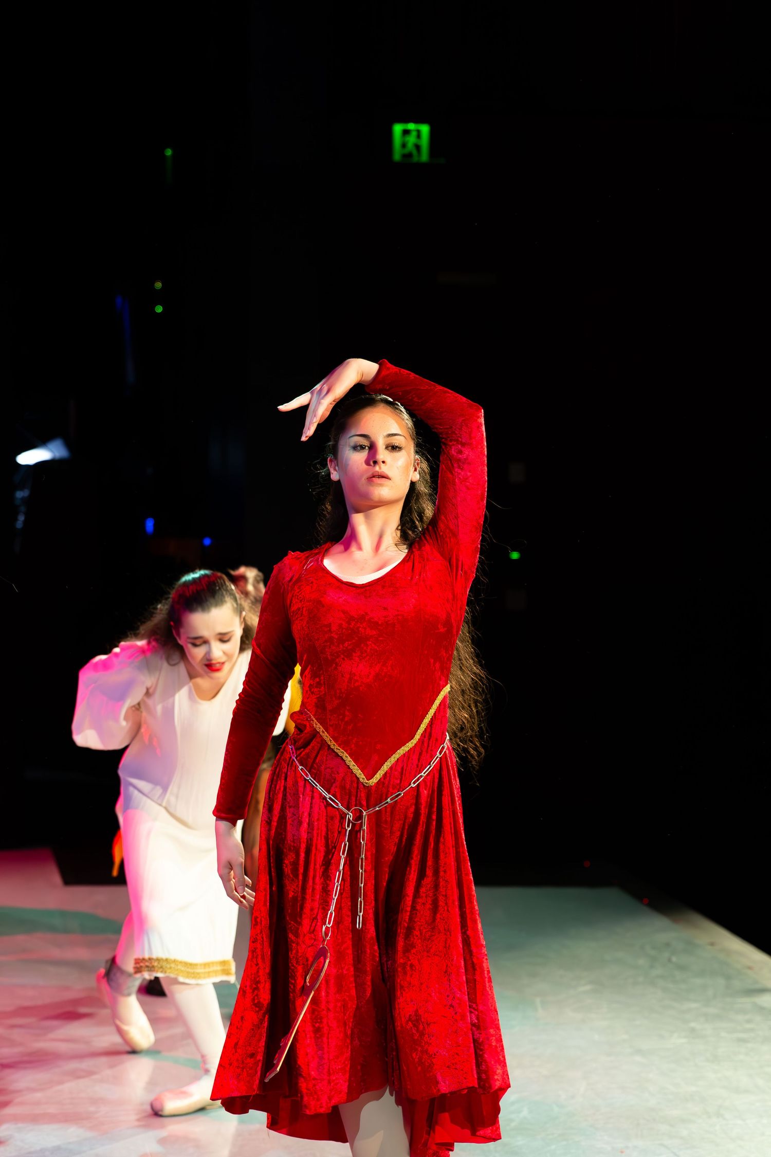 Woman in red dress performs flamenco dance on stage with another dancer in white behind her.