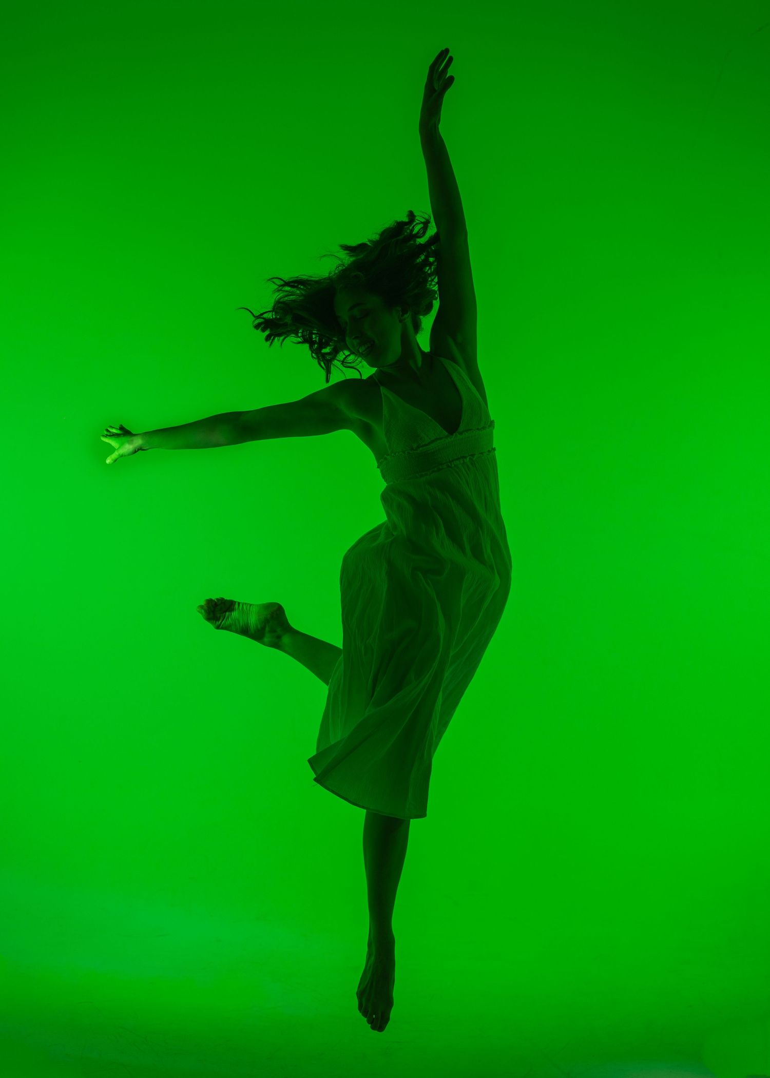 Silhouette of a female dancer leaping gracefully against a vibrant green background in a flowing white dress.