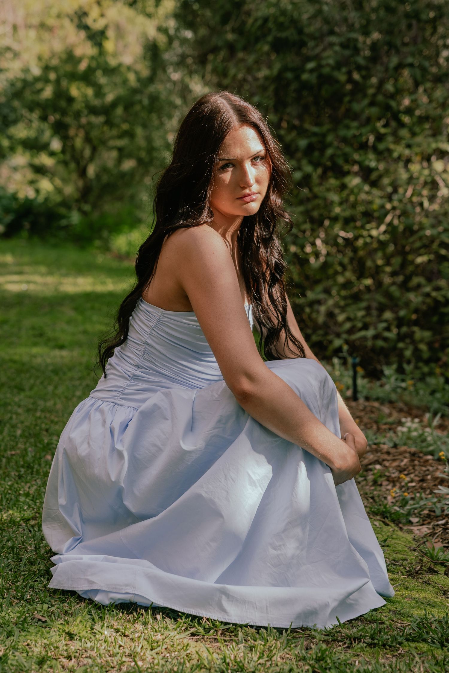 Young woman in white dress sitting on grass in garden.