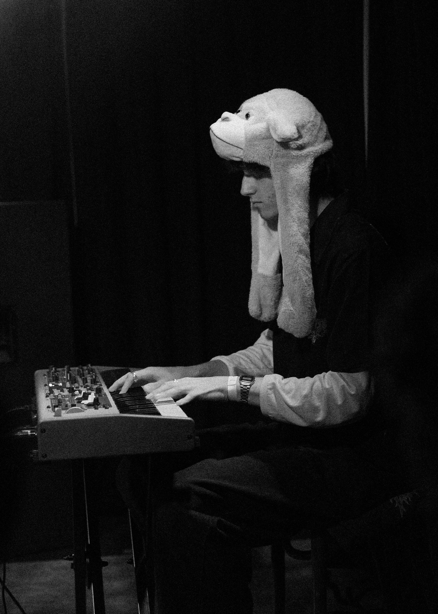 Keyboard player wearing a novelty stuffed animal hat performs on synthesizer in black and white photo.