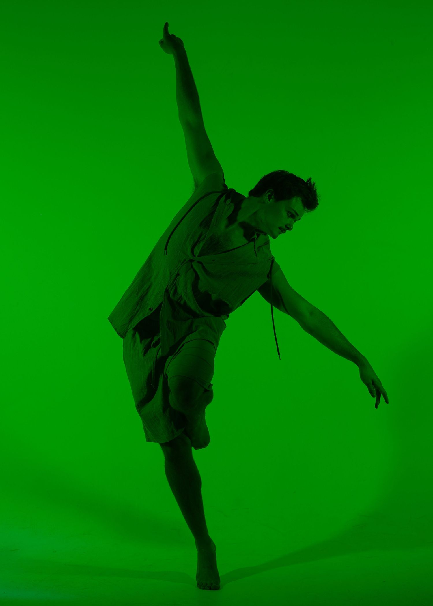 Dancer in green light leaning back with one arm raised performing contemporary dance pose against green background.