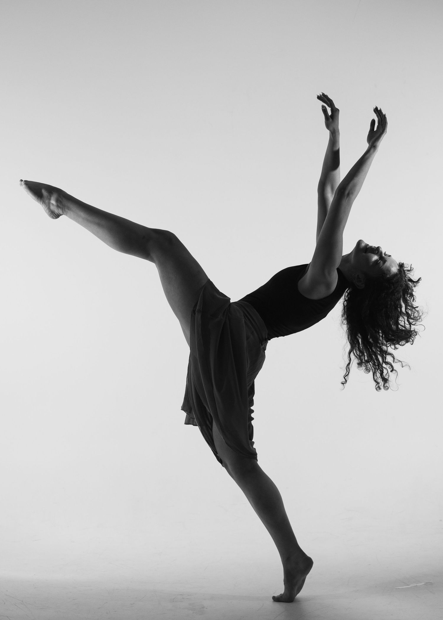 Silhouette of a dancer performing a high kick in a dramatic black and white photo.