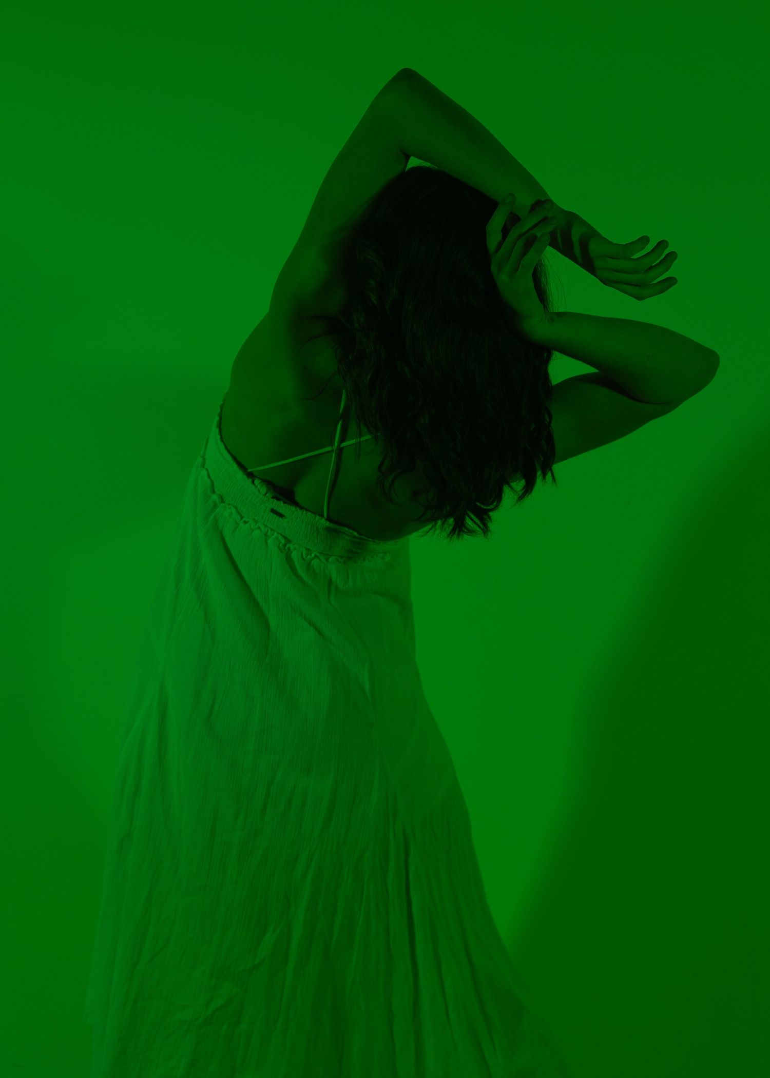 Artistic silhouette of a woman in a white dress dancing against a vibrant green background.