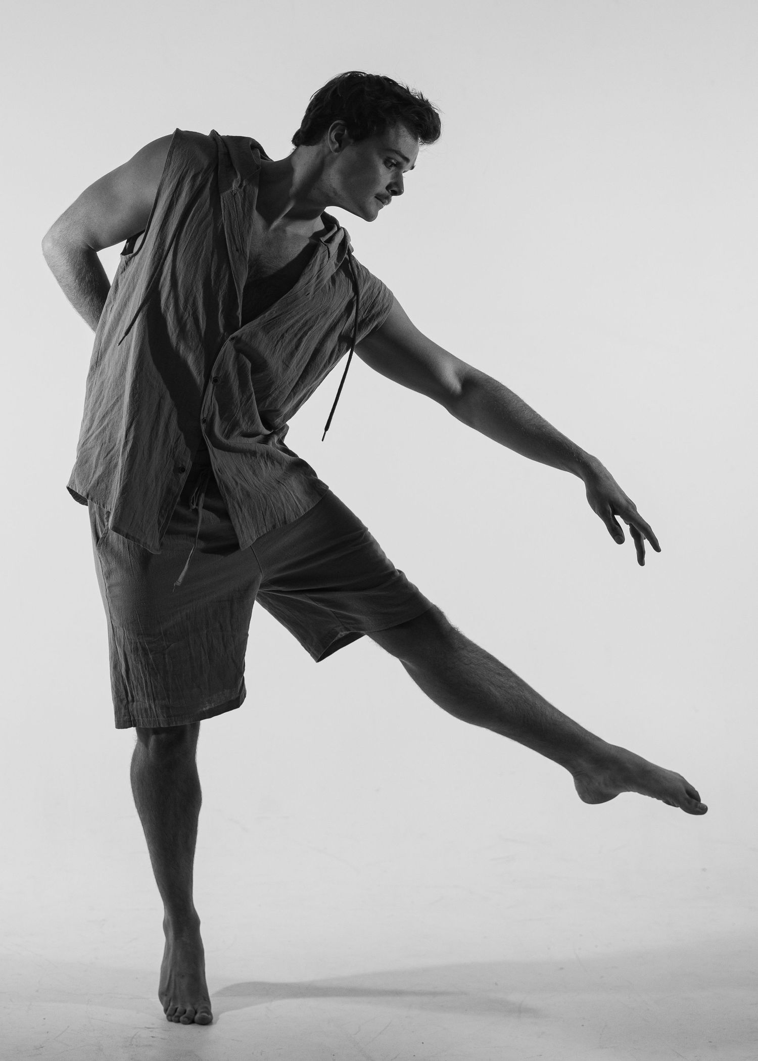Male dancer performs elegant contemporary dance pose in black and white studio photo.