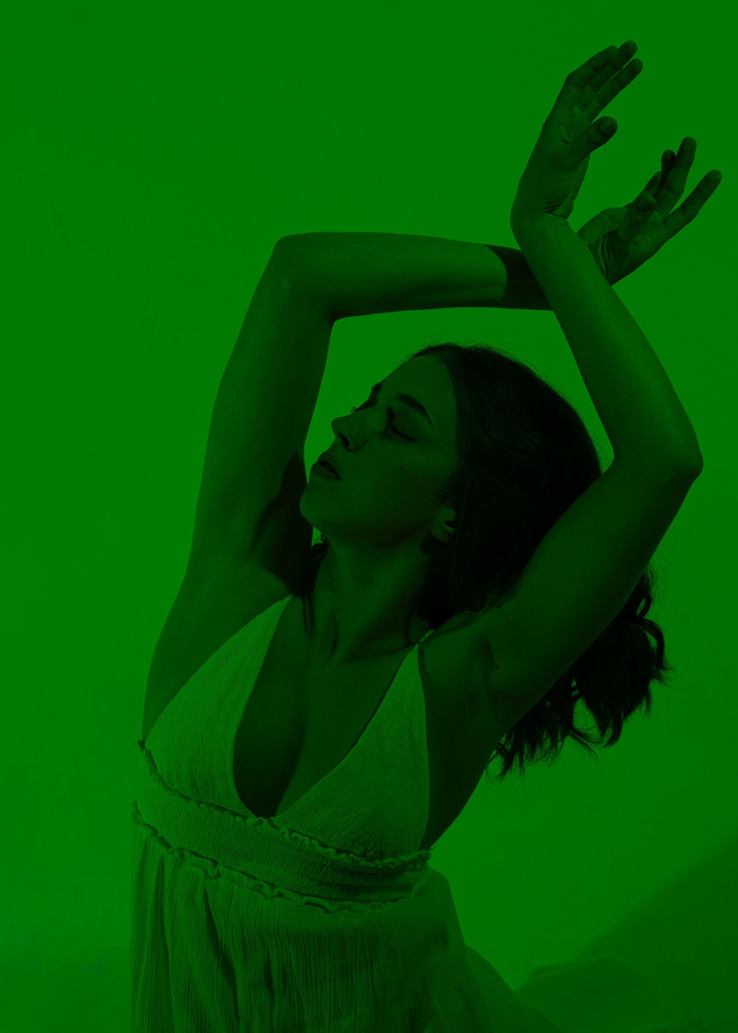 Woman dancing gracefully with arms raised overhead, bathed in dramatic green light.