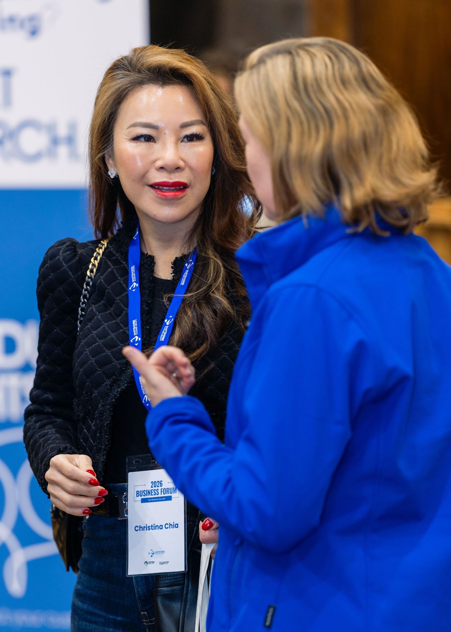 Two women networking at a business forum conference, one wearing a blue lanyard name badge reading Christina Chia.