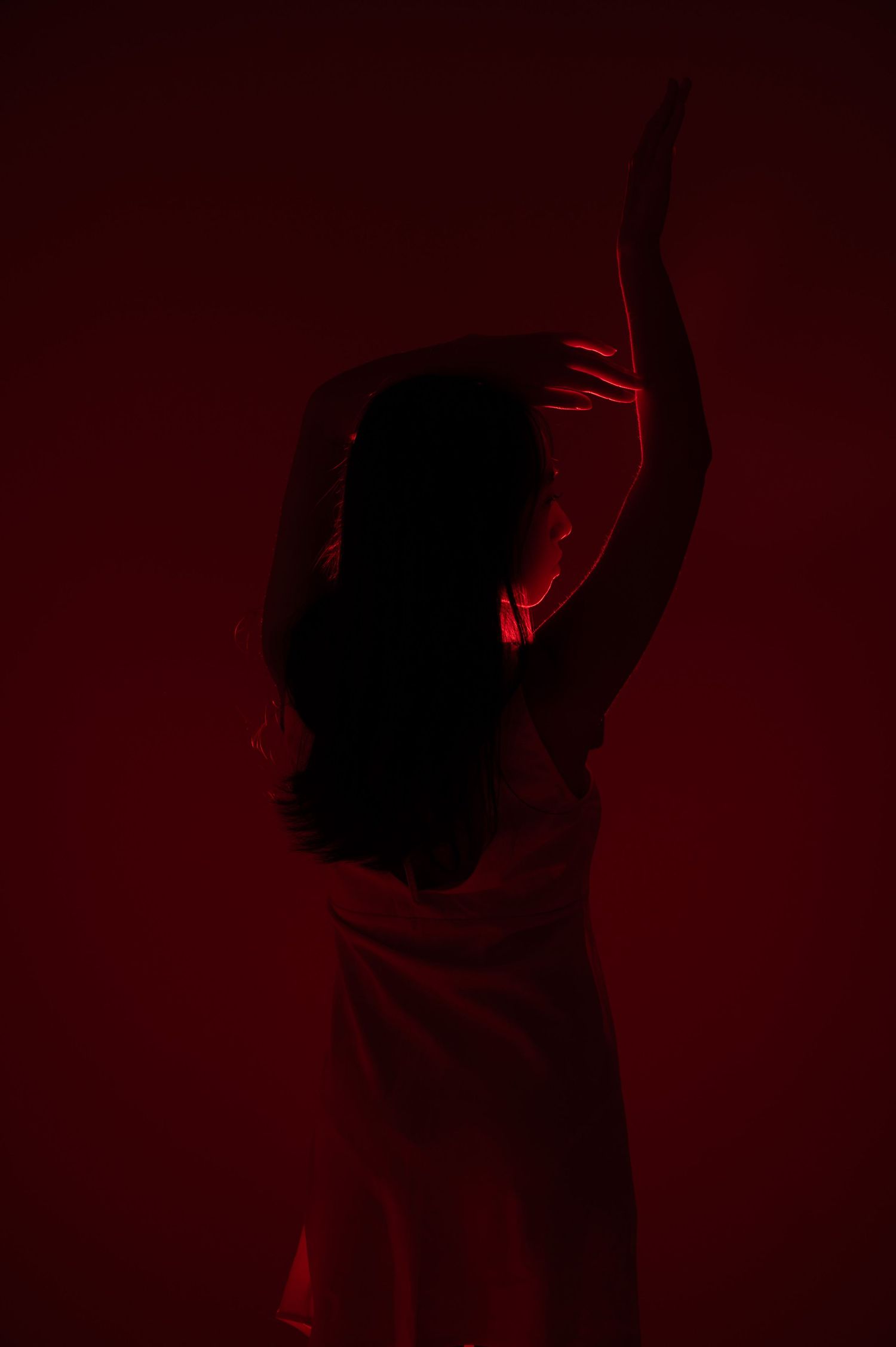Silhouetted dancer performs expressive movements against deep red background.