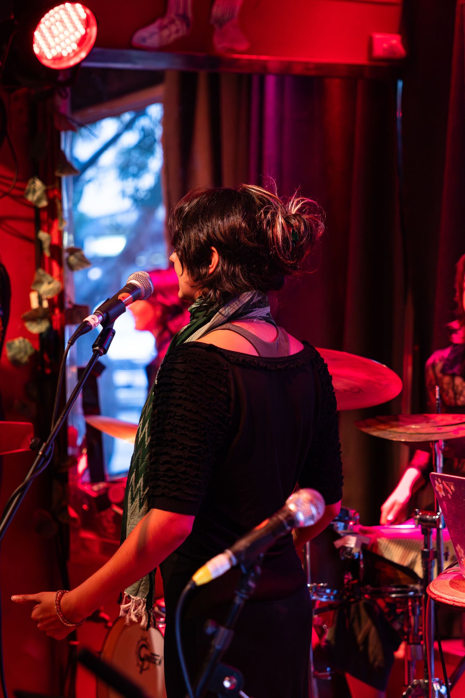 Musicians perform on stage in a dark venue illuminated by dramatic red lighting and blue accents.