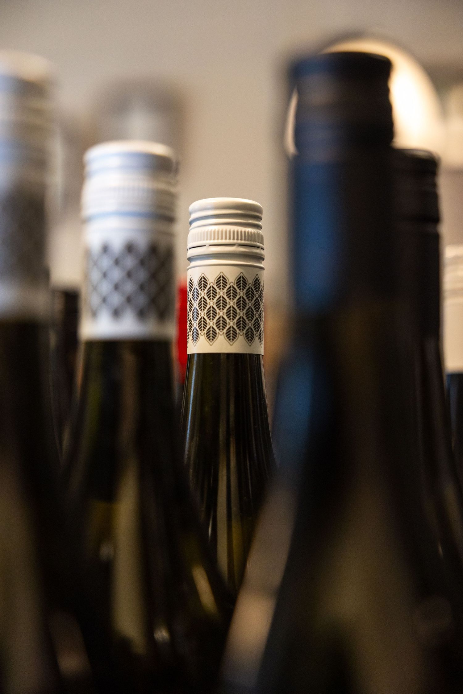 Close-up of wine bottle tops with decorative capsules and screw caps arranged in a row.