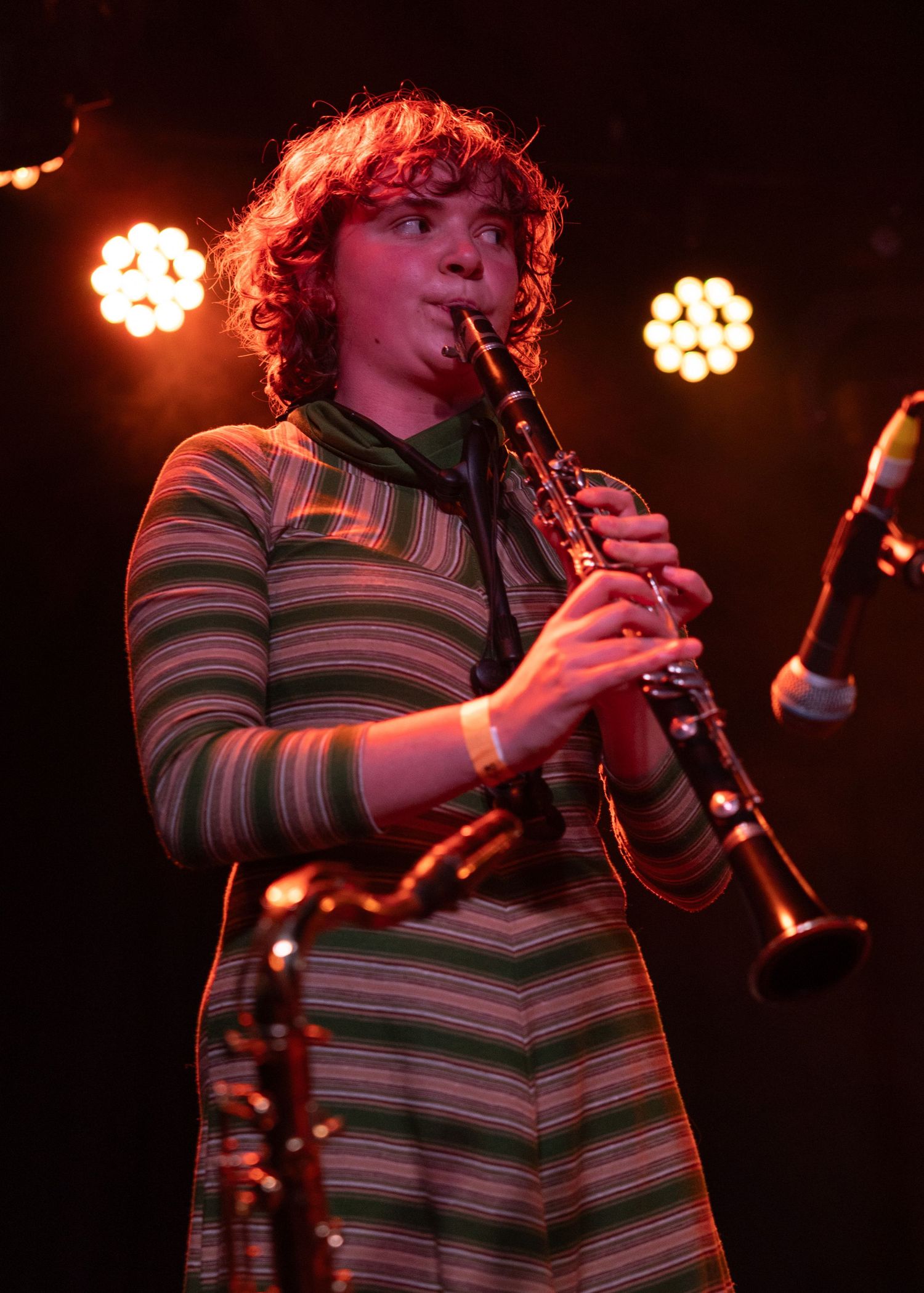 Young musician playing clarinet on stage under warm red stage lights wearing a striped green dress.