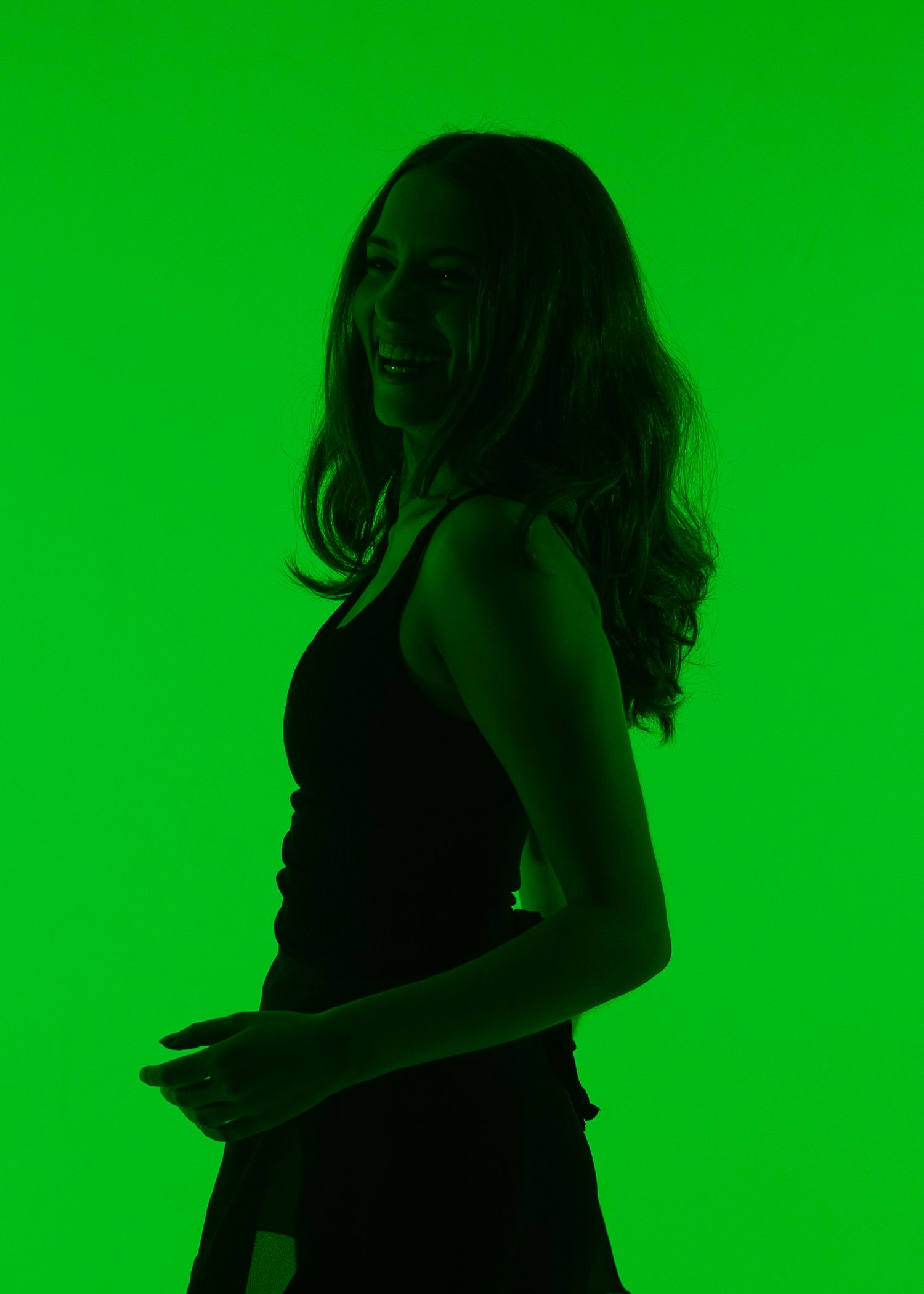 Silhouette of a smiling woman with long wavy hair posing against a vibrant green background.