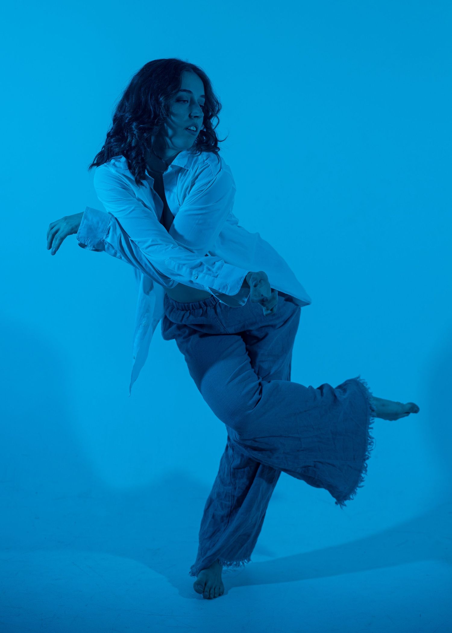 Woman dancing expressively in blue-toned light wearing wide-leg frayed pants and white shirt.