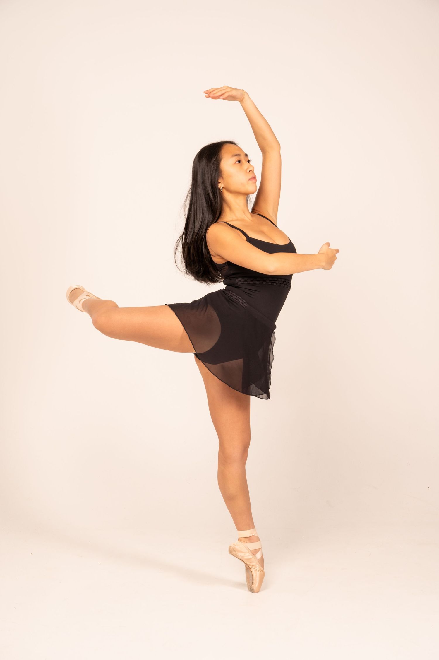 Ballet dancer in black dress executes elegant arabesque poses in studio setting.
