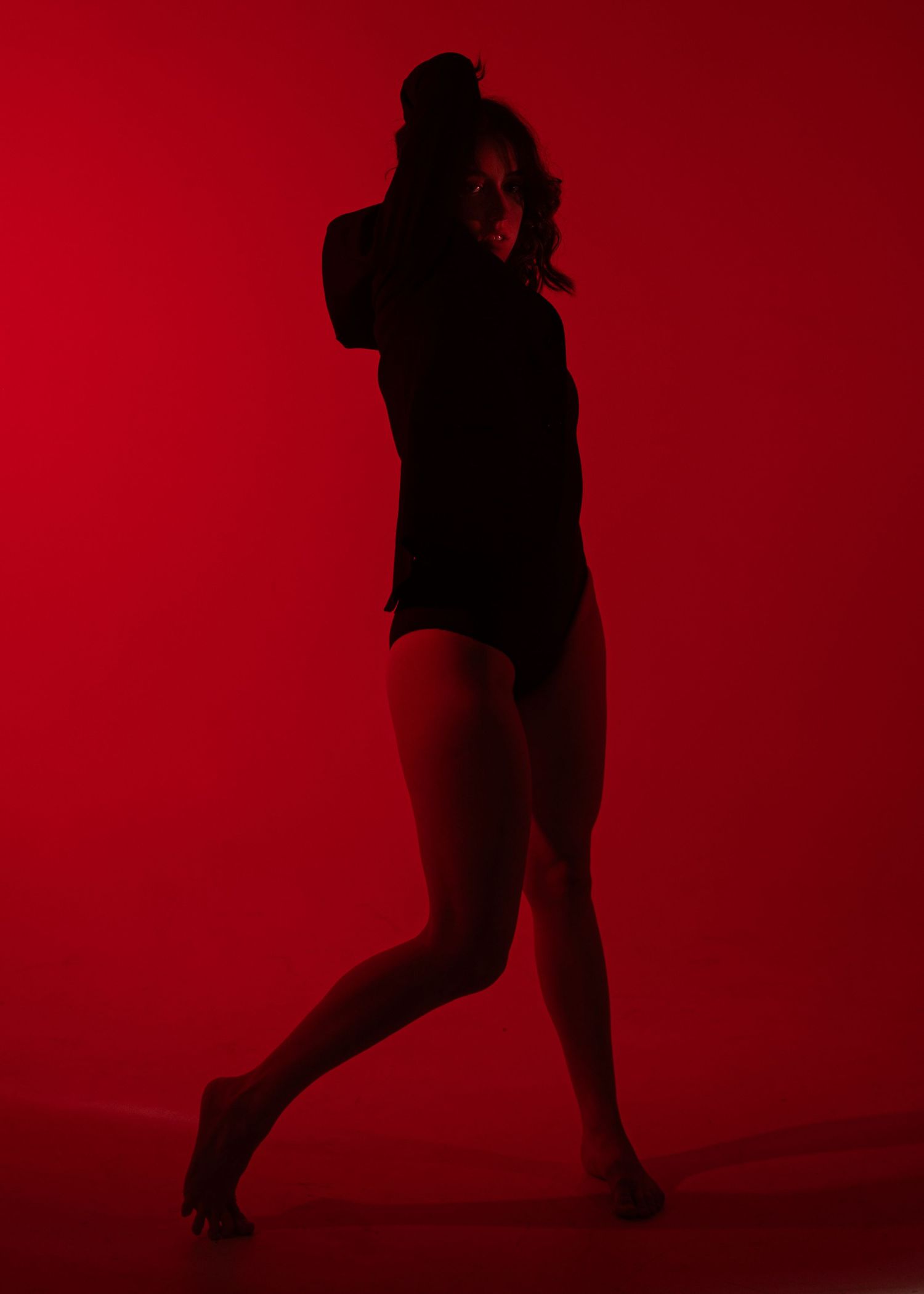 Dramatic silhouette of female dancer posing against vibrant red background in dark studio lighting.