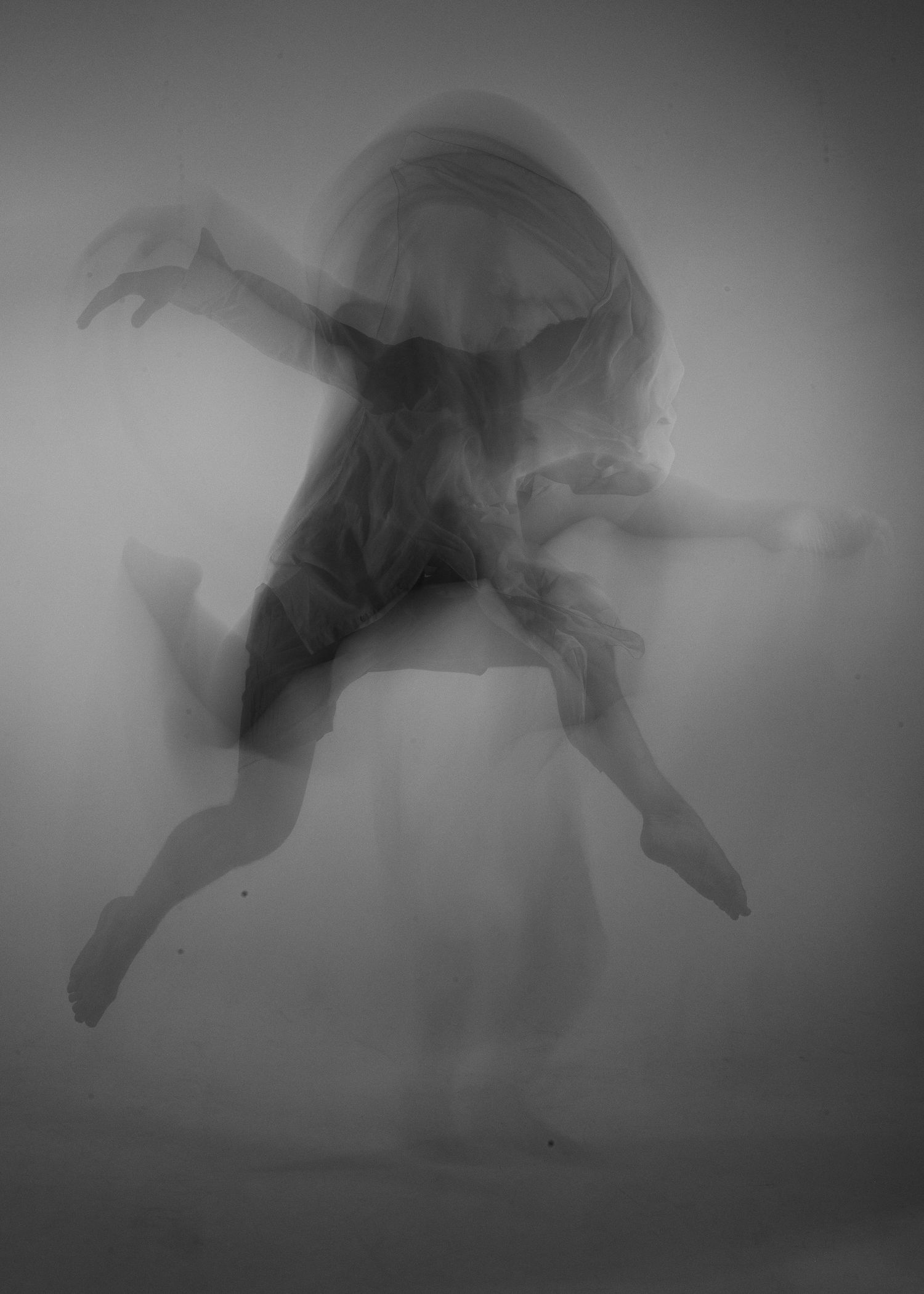 Ghostly black and white long exposure photo of a dancer mid-leap, creating ethereal motion blur effect.